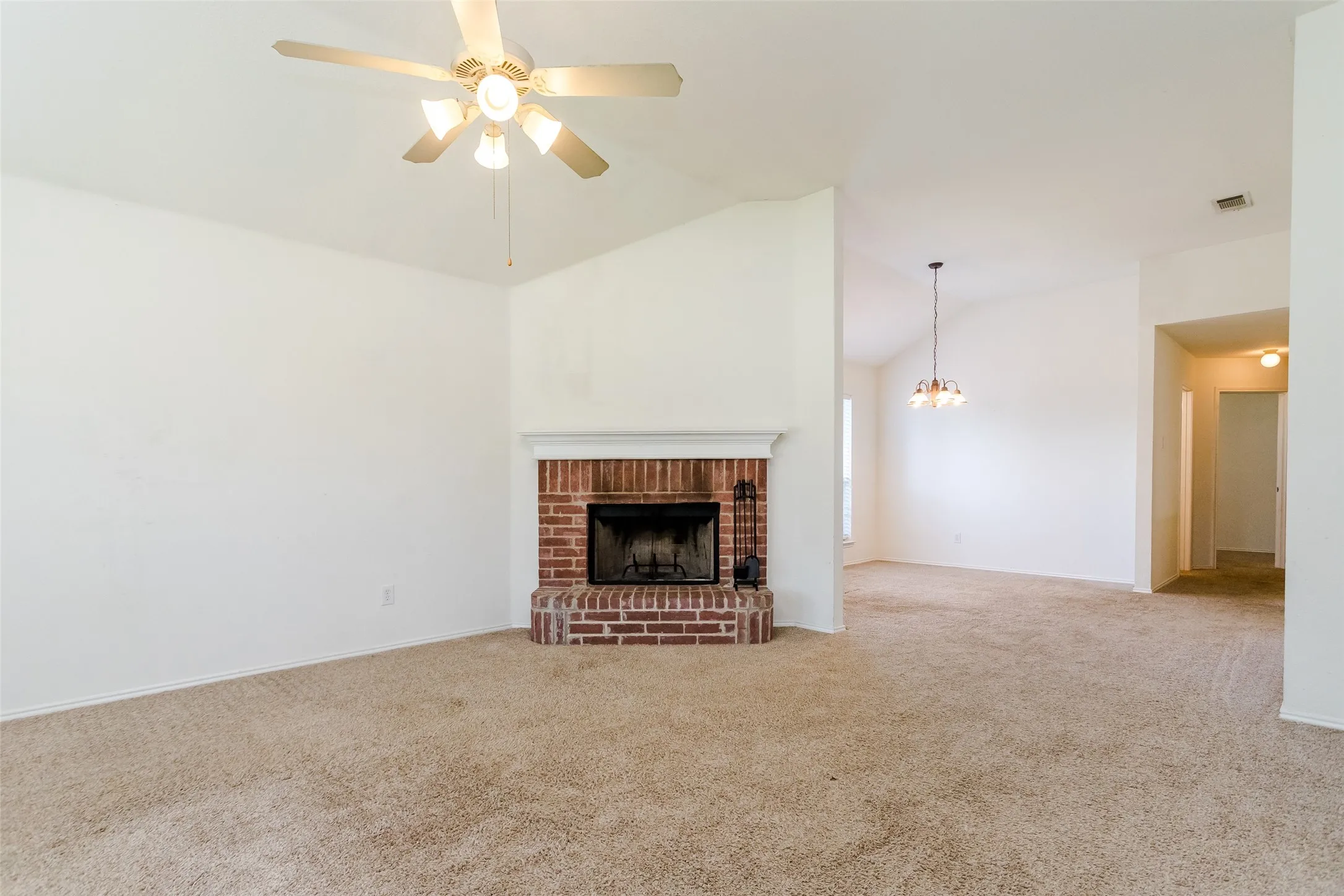 Unfurnished living room with carpet floors, a brick fireplace, ceiling fan with notable chandelier, and high vaulted ceiling