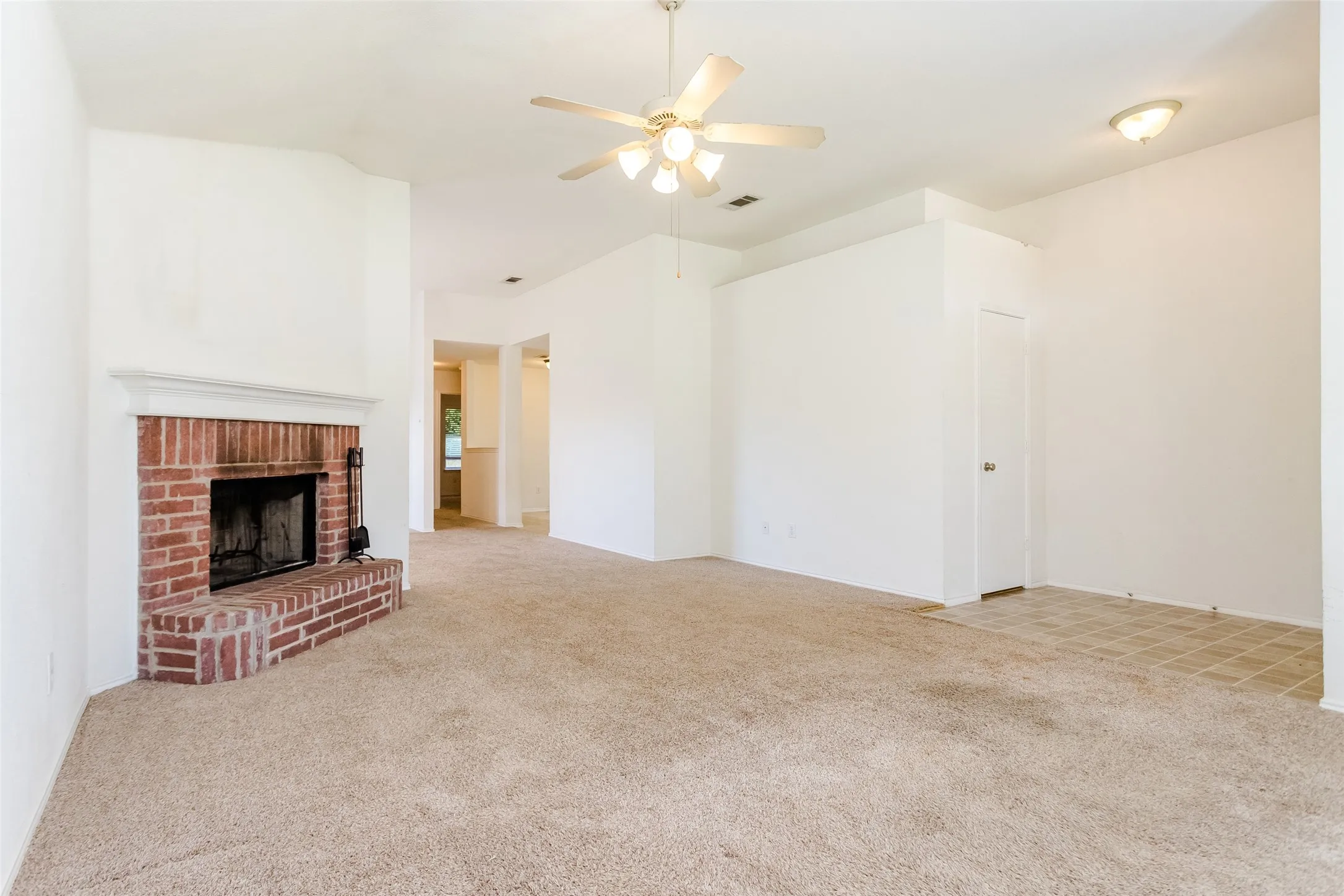 Unfurnished living room featuring ceiling fan, light carpet, and a brick fireplace