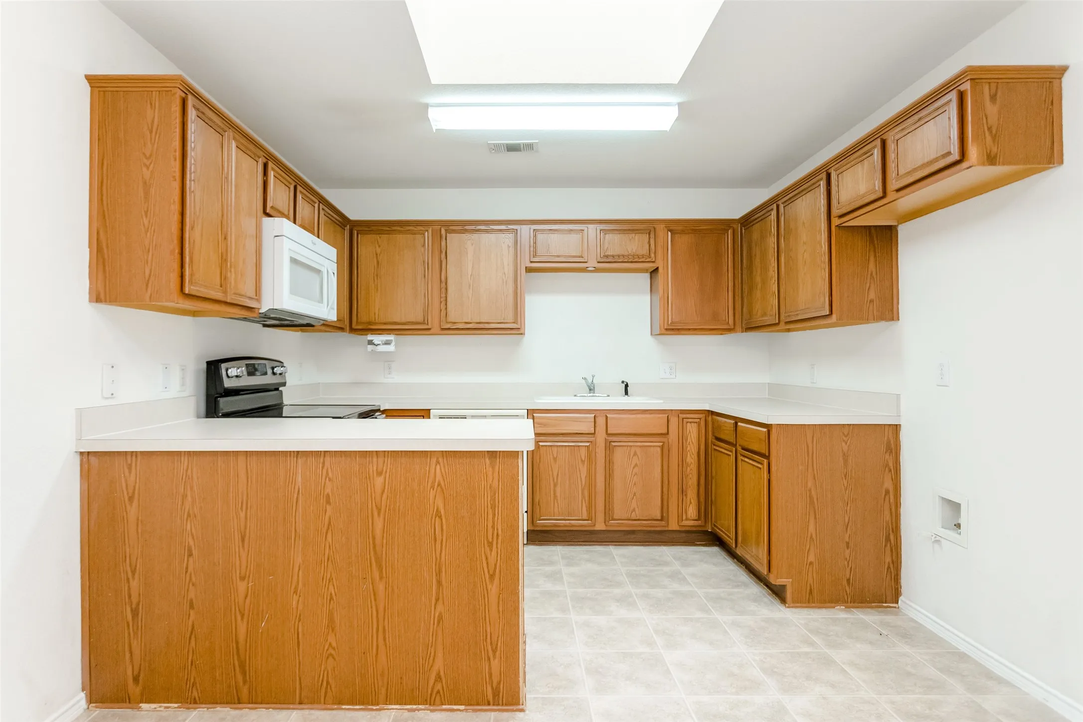 Kitchen with kitchen peninsula, sink, light tile patterned floors, and range with electric cooktop