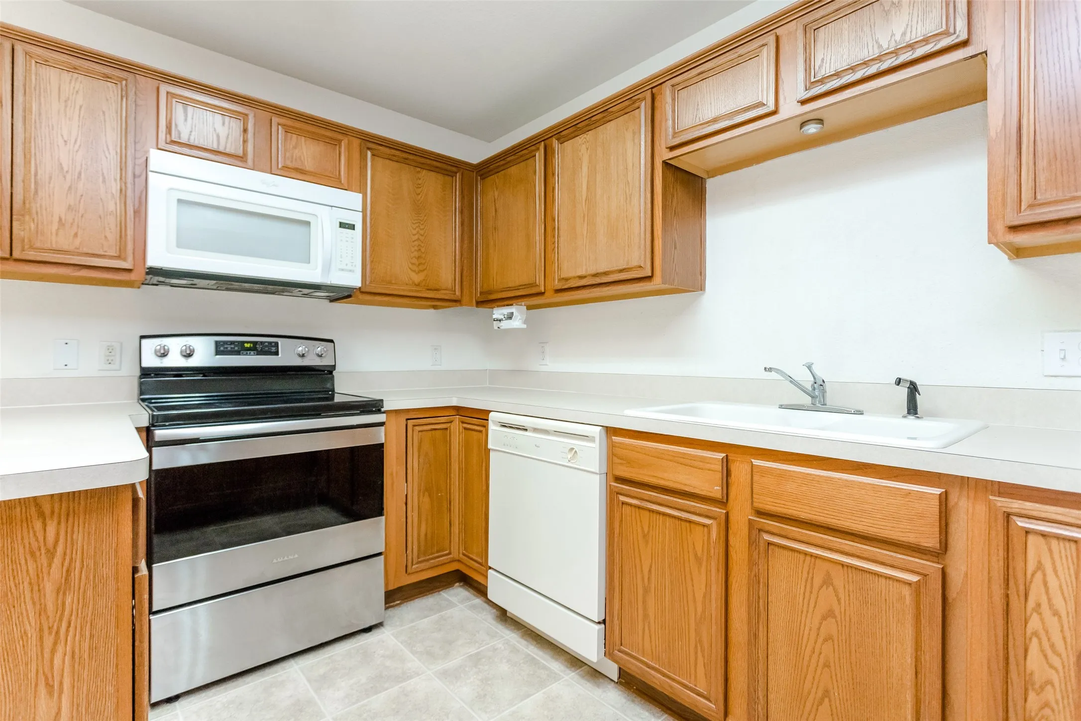 Kitchen with light tile patterned floors, white appliances, and sink