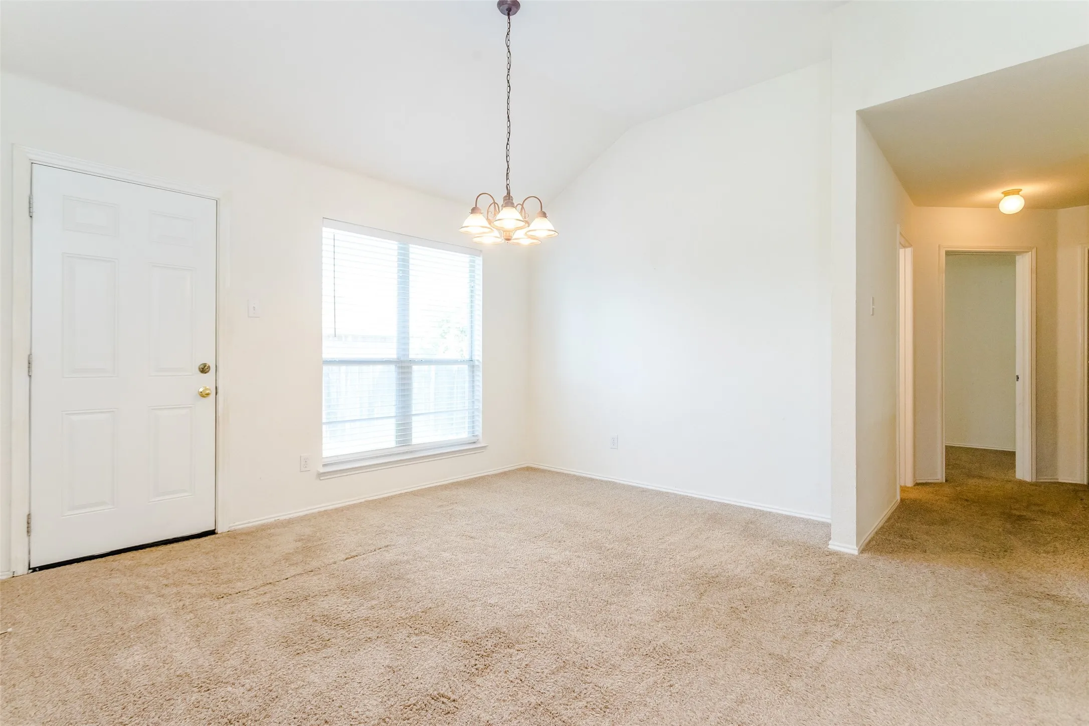 Empty room with a notable chandelier, carpet, and vaulted ceiling