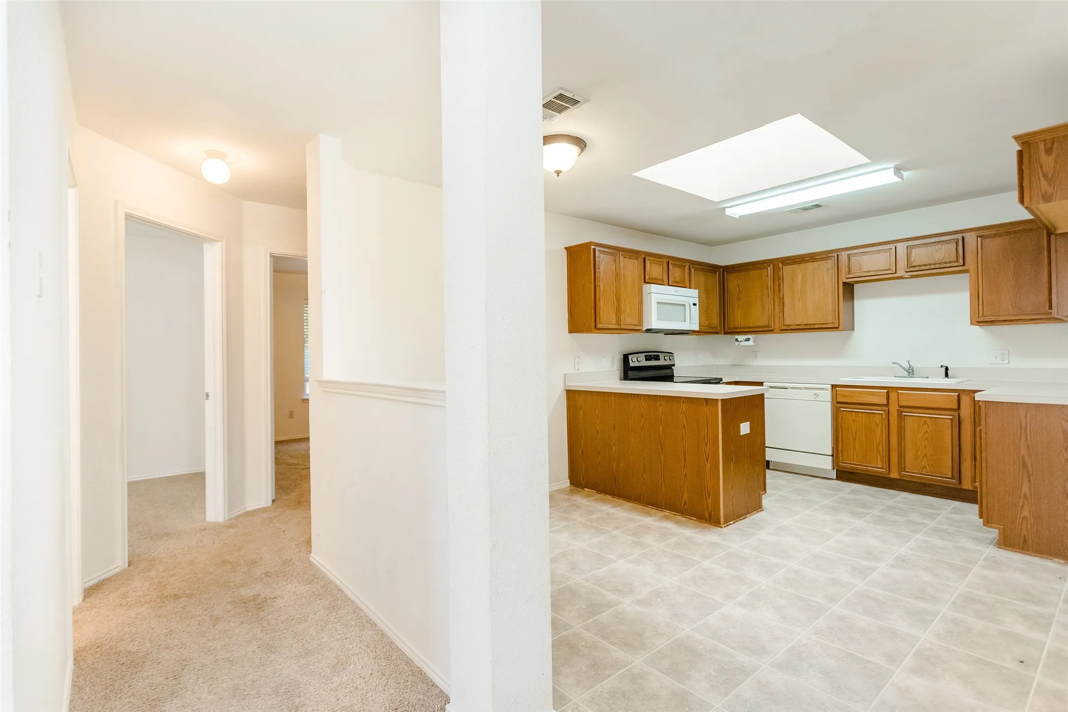 Kitchen featuring a skylight, sink, light carpet, and white appliances