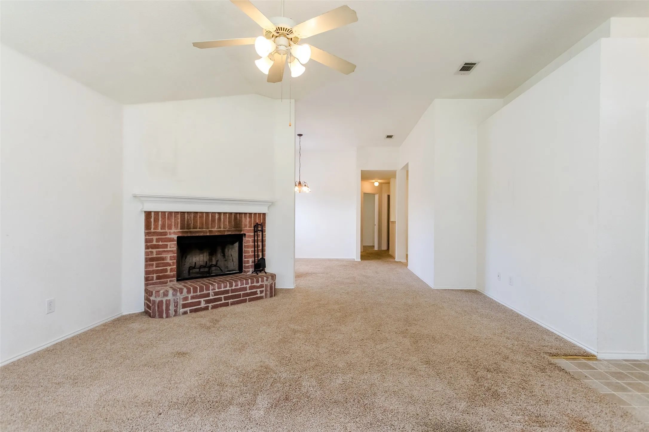 Unfurnished living room featuring carpet flooring, lofted ceiling, a brick fireplace, and ceiling fan