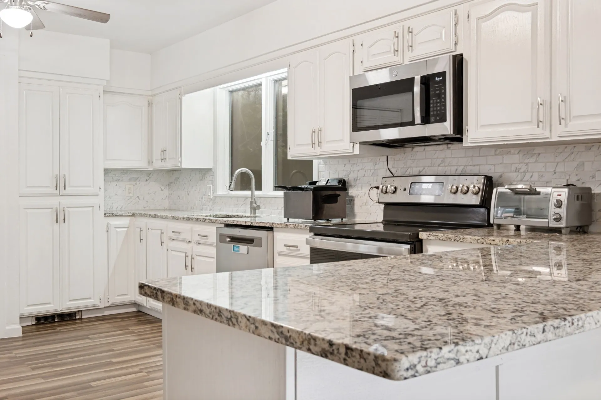 Chef's kitchen featuring white cabinetry, granite countertops, stainless steel appliances including a gas range and over-the-range microwave, subway tile backsplash, and an island with extended seating