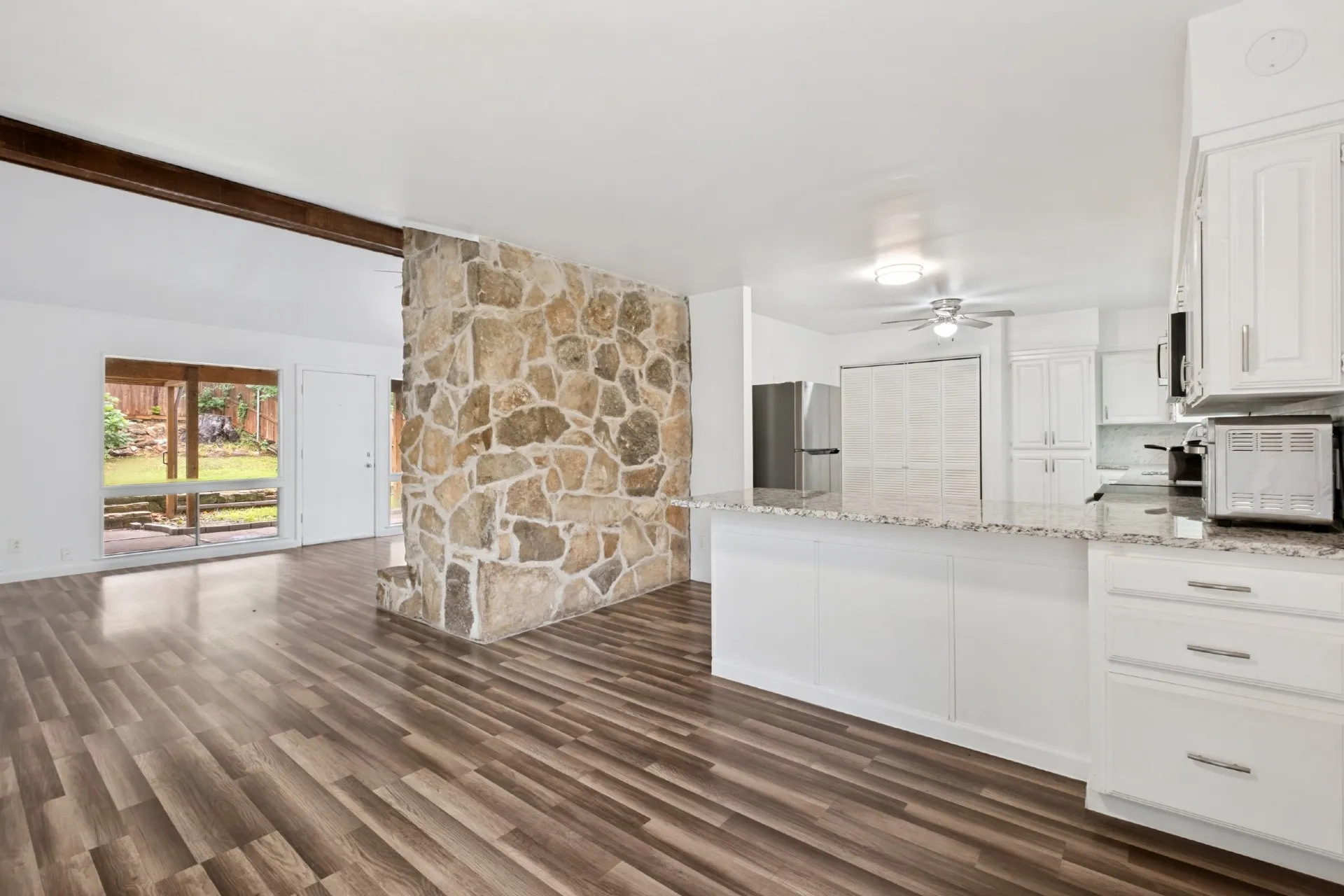 Wood-finish flooring throughout, a stone-accented wall, and white cabinetry with stainless hardware