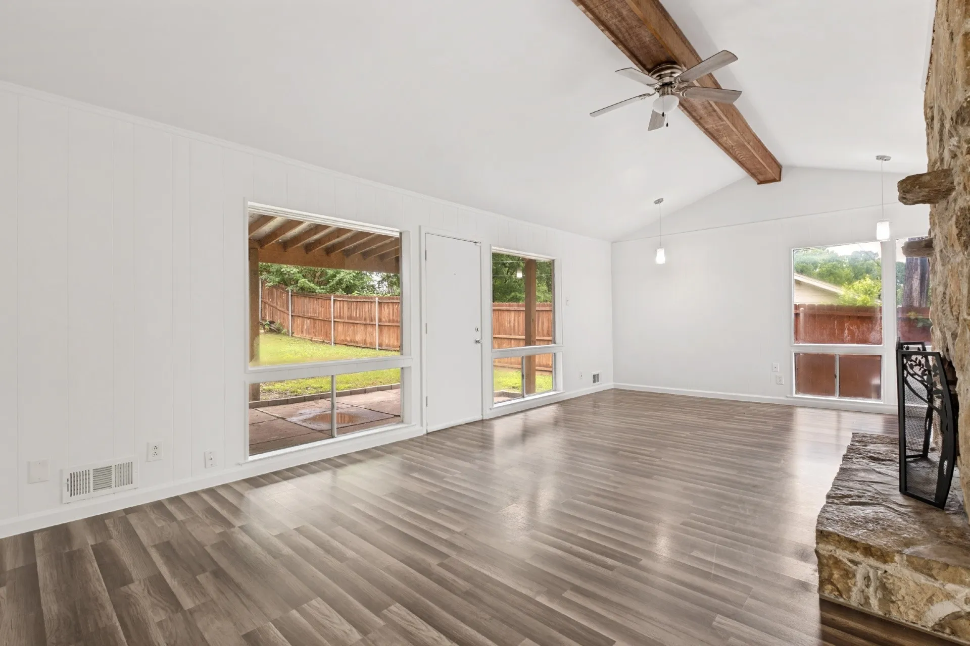 Spacious living area featuring vaulted ceilings, exposed wood beam, a stone-clad fireplace, wood-finish flooring, and multiple windows