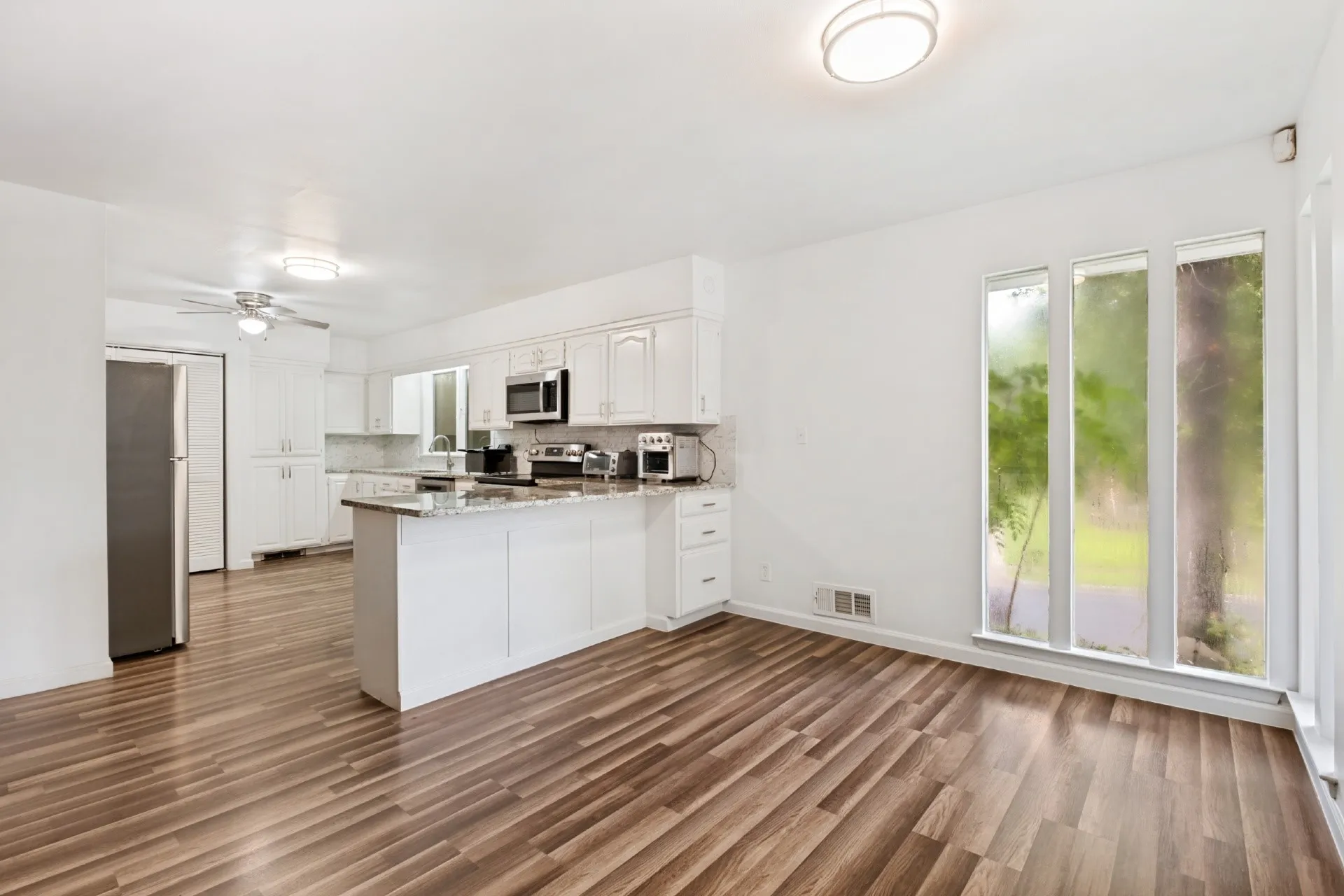 White cabinetry with stainless steel appliances, wood-finish flooring, a kitchen island with a stone countertop, and large vertical windows