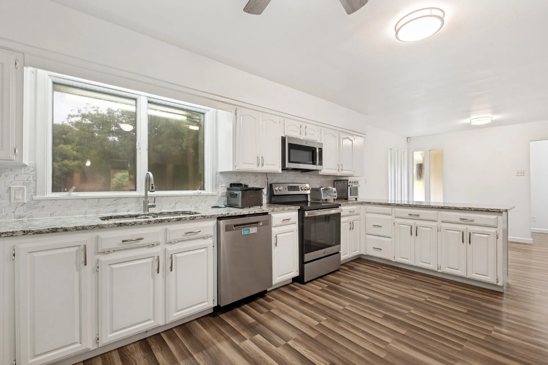 Kitchen featuring white cabinetry, stainless steel appliances, speckled stone countertops, and wood-finish flooring