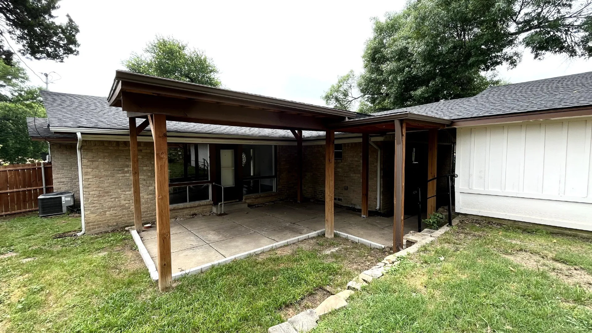 Covered concrete patio with wood support beams and brick exterior