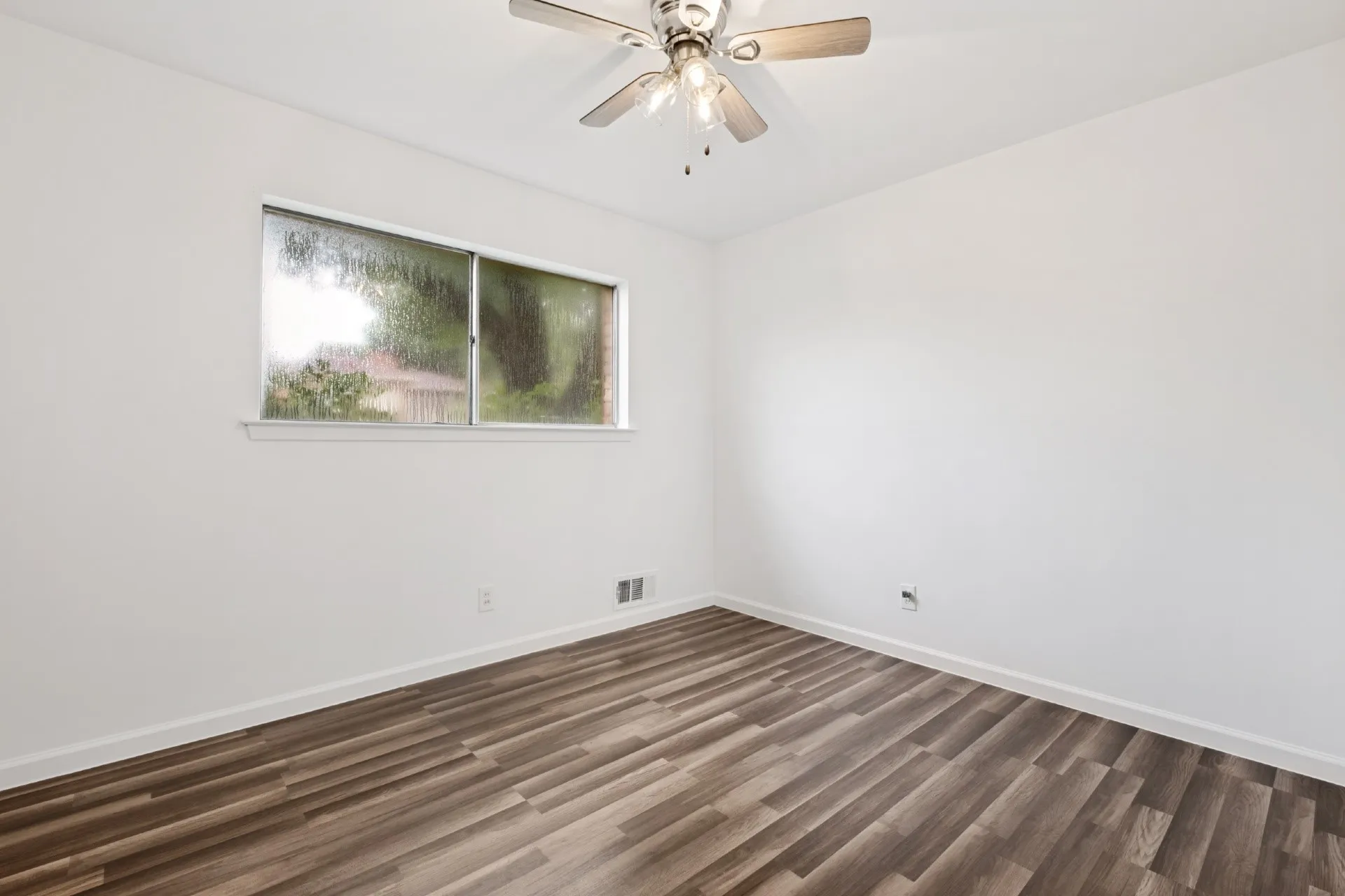 Bright, light-filled bedroom showcasing newly installed wood-finish flooring, ceiling fan with integrated lighting, and large transom window providing natural illumination