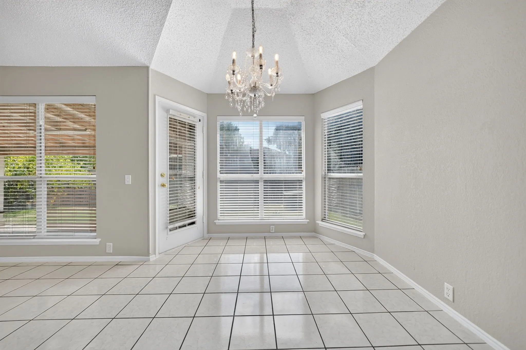 Vaulted ceiling with a chandelier, bay window, multiple windows with blinds, and tile flooring