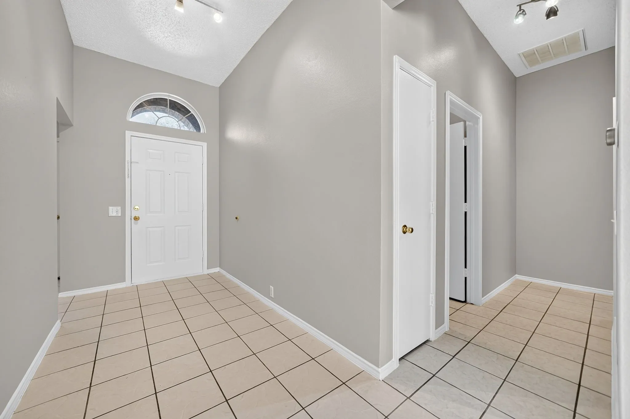 Vaulted ceiling, arched transom window, ceramic tile flooring, neutral wall tones, and white paneled doors