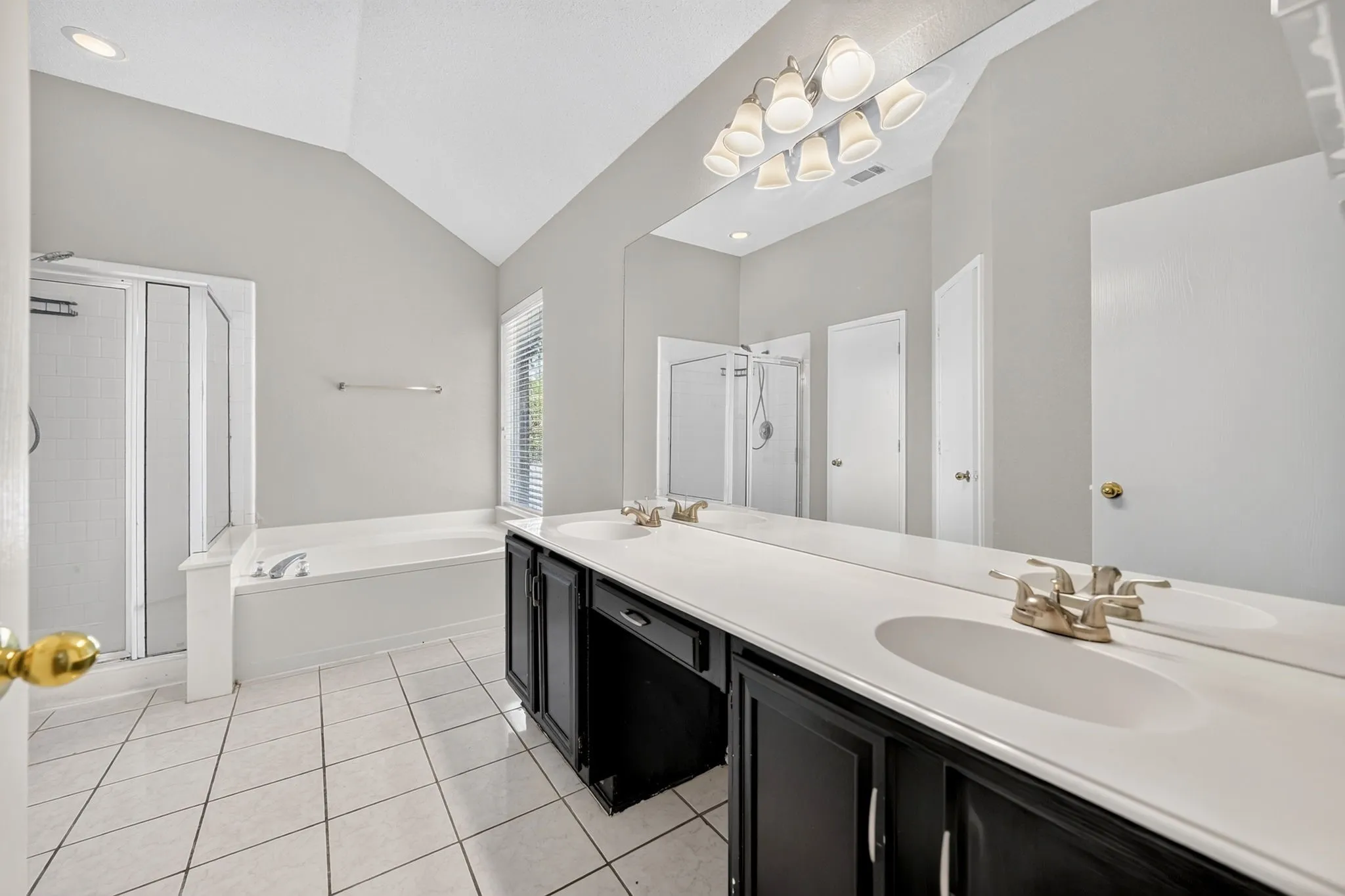 Vaulted ceiling bathroom featuring a double vanity, large soaking tub, separate shower enclosure, and tiled flooring