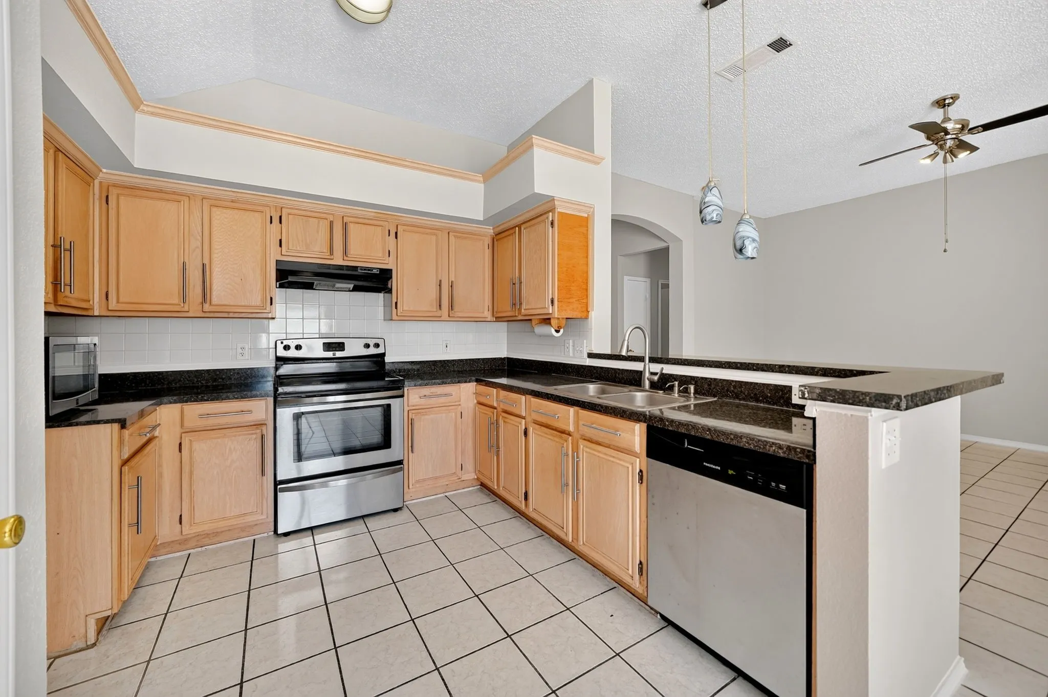 Kitchen featuring wood cabinetry, dark countertops, a tile backsplash, stainless steel appliances, and tile flooring