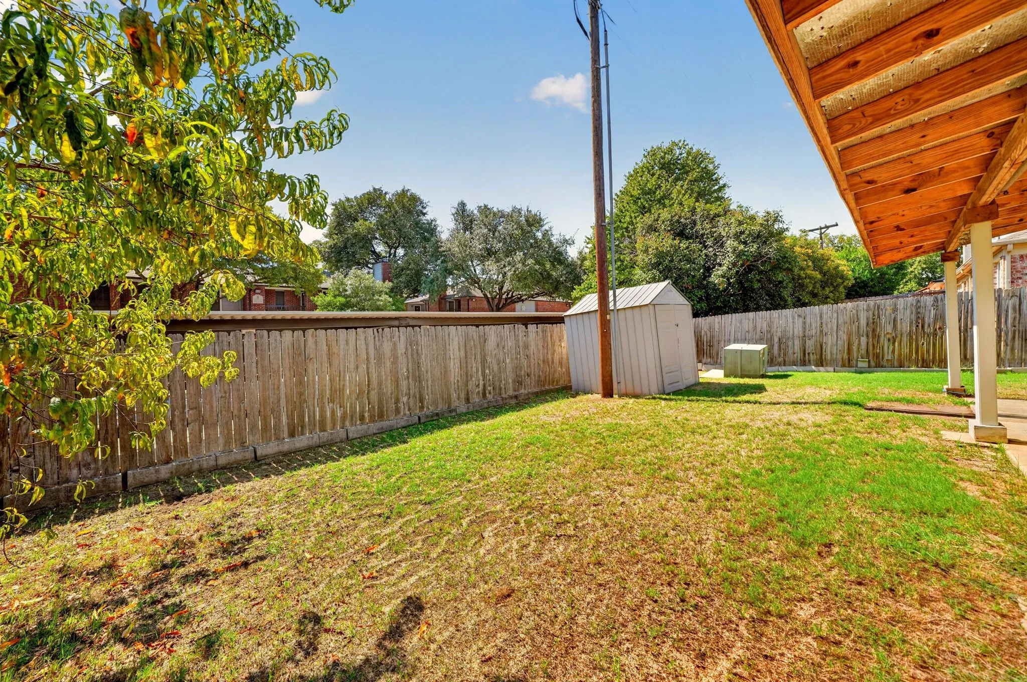 Expansive backyard featuring a wood fence, storage shed, and covered patio with exposed wood ceiling