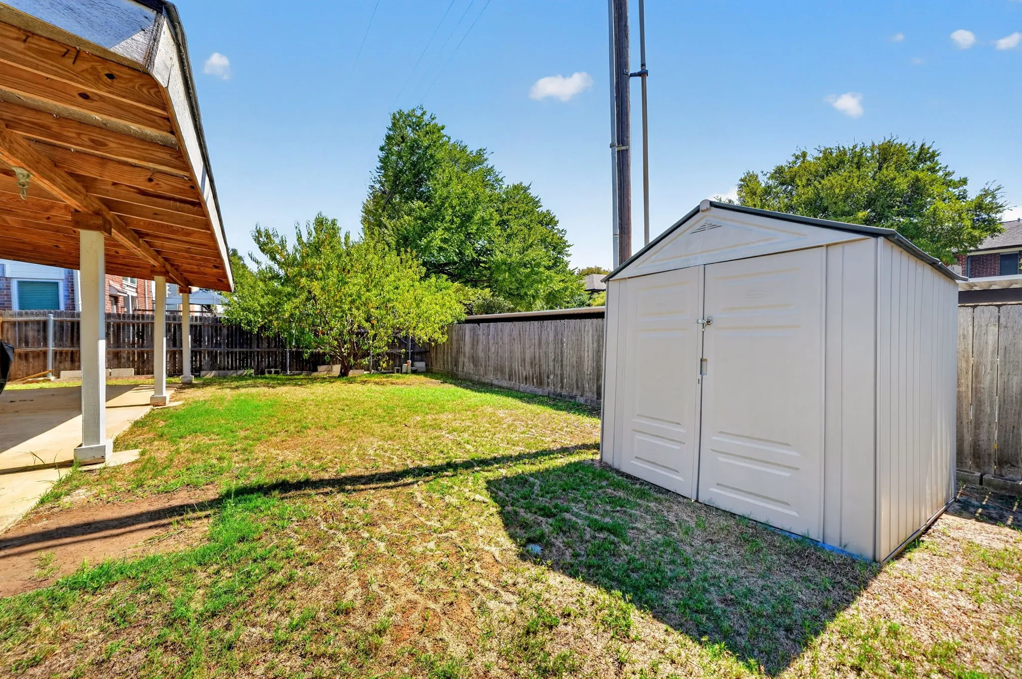 Fenced backyard featuring a covered patio with exposed wood ceiling, a storage shed, and mature trees