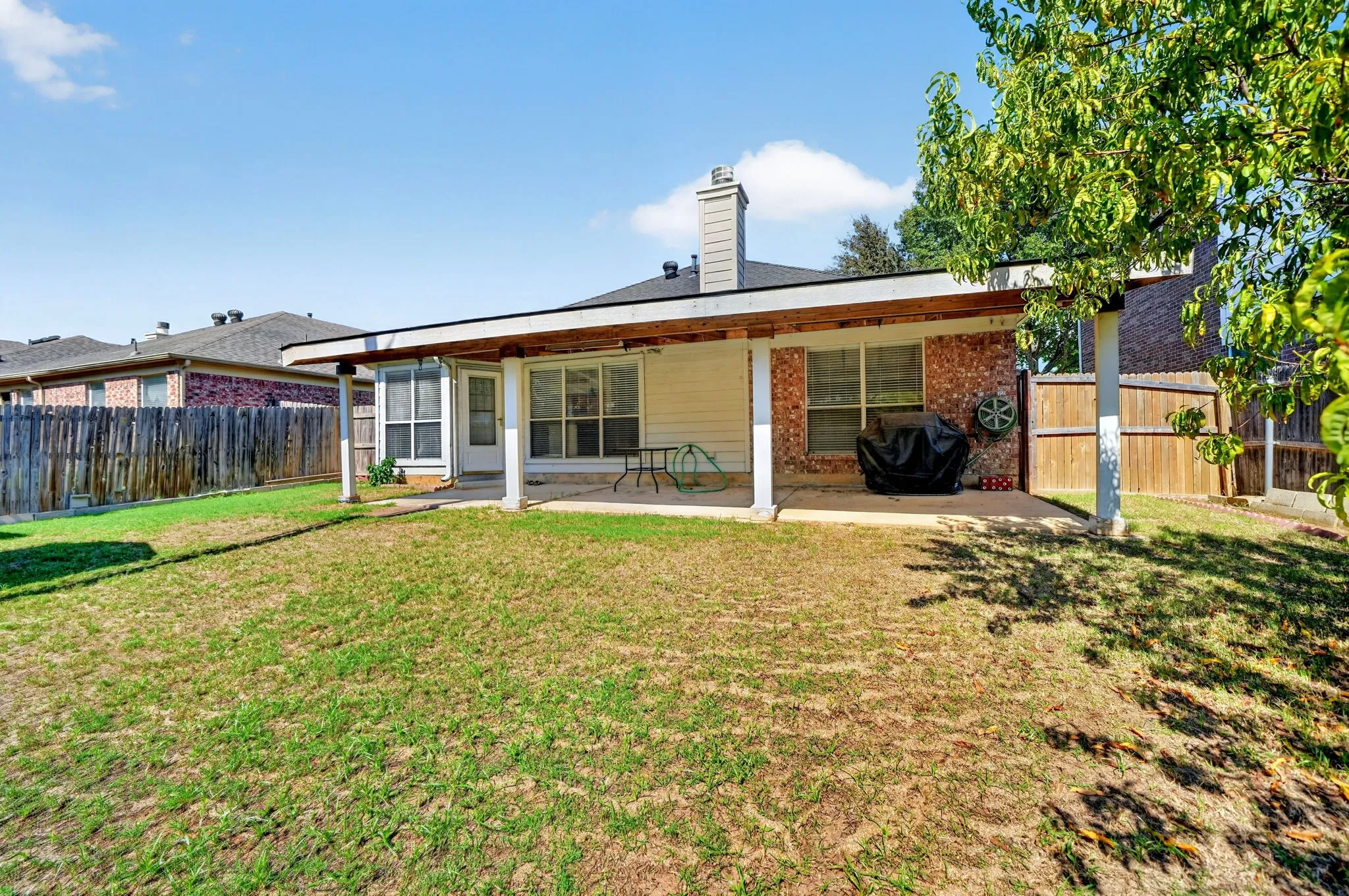 Extended covered patio with a concrete surface, brick exterior accents, and a wood privacy fence