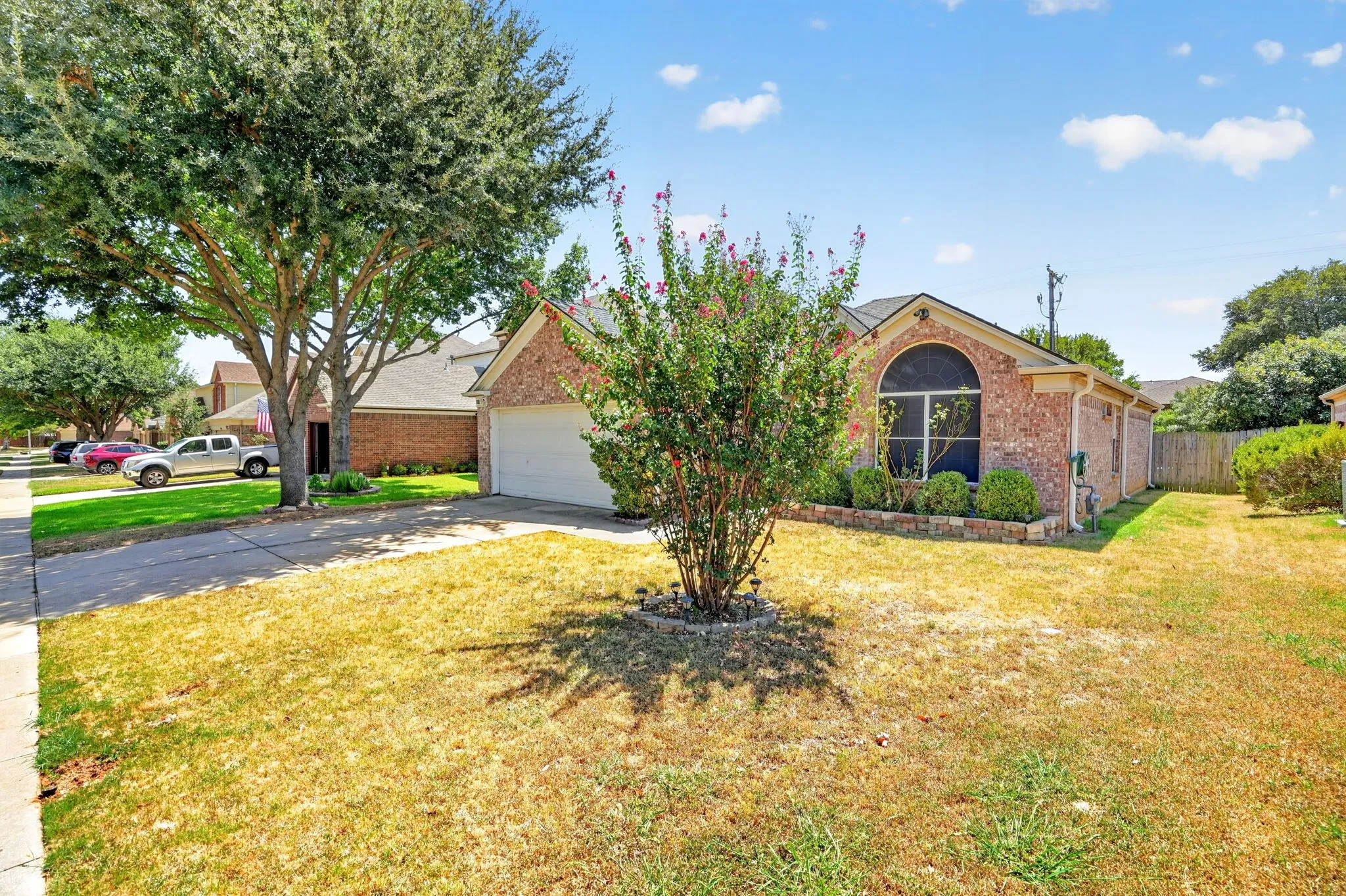 Brick exterior, arched window, attached garage, mature front yard tree, and landscaping