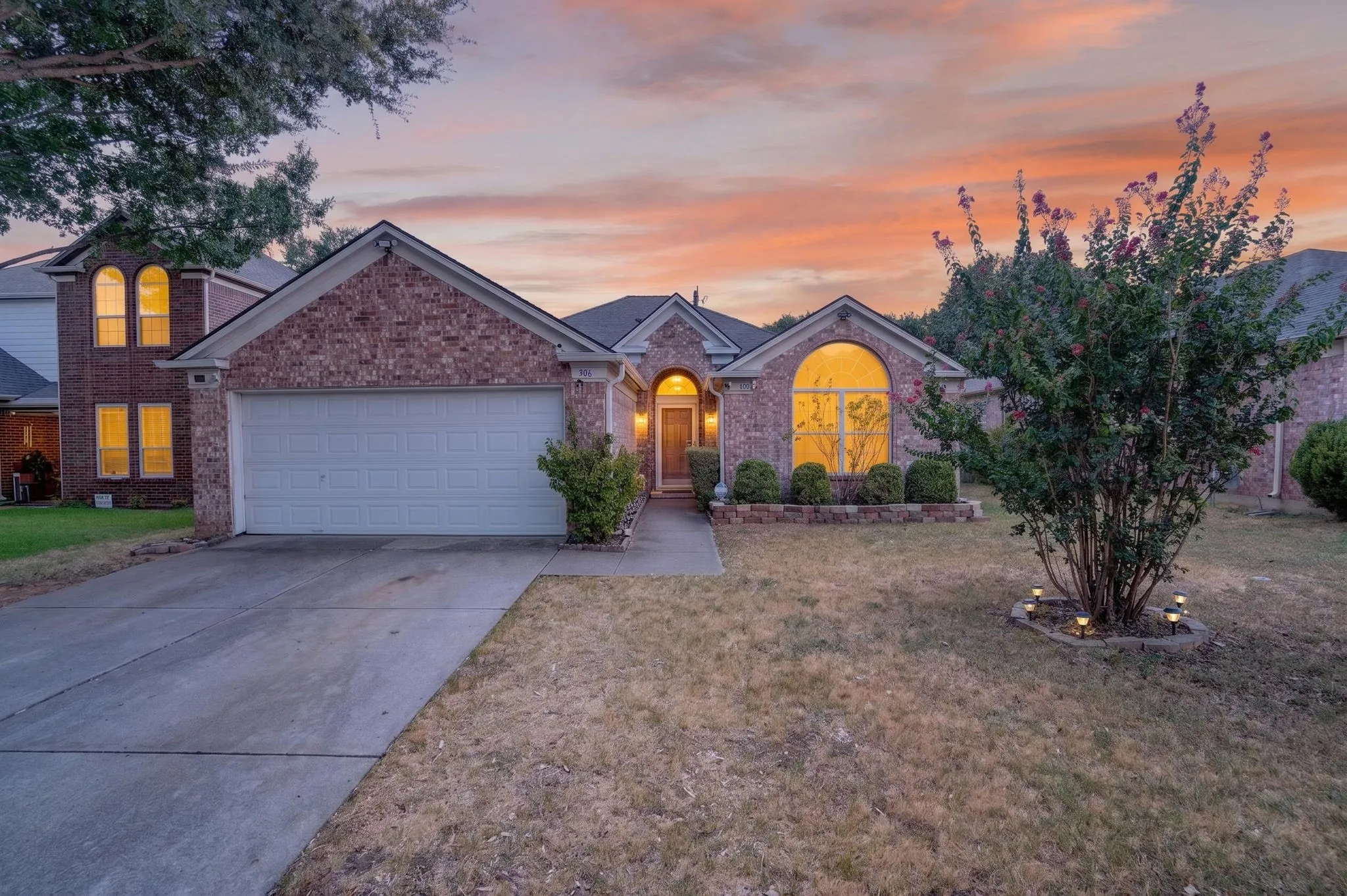Brick exterior with an arched window, attached two-car garage, and a concrete driveway