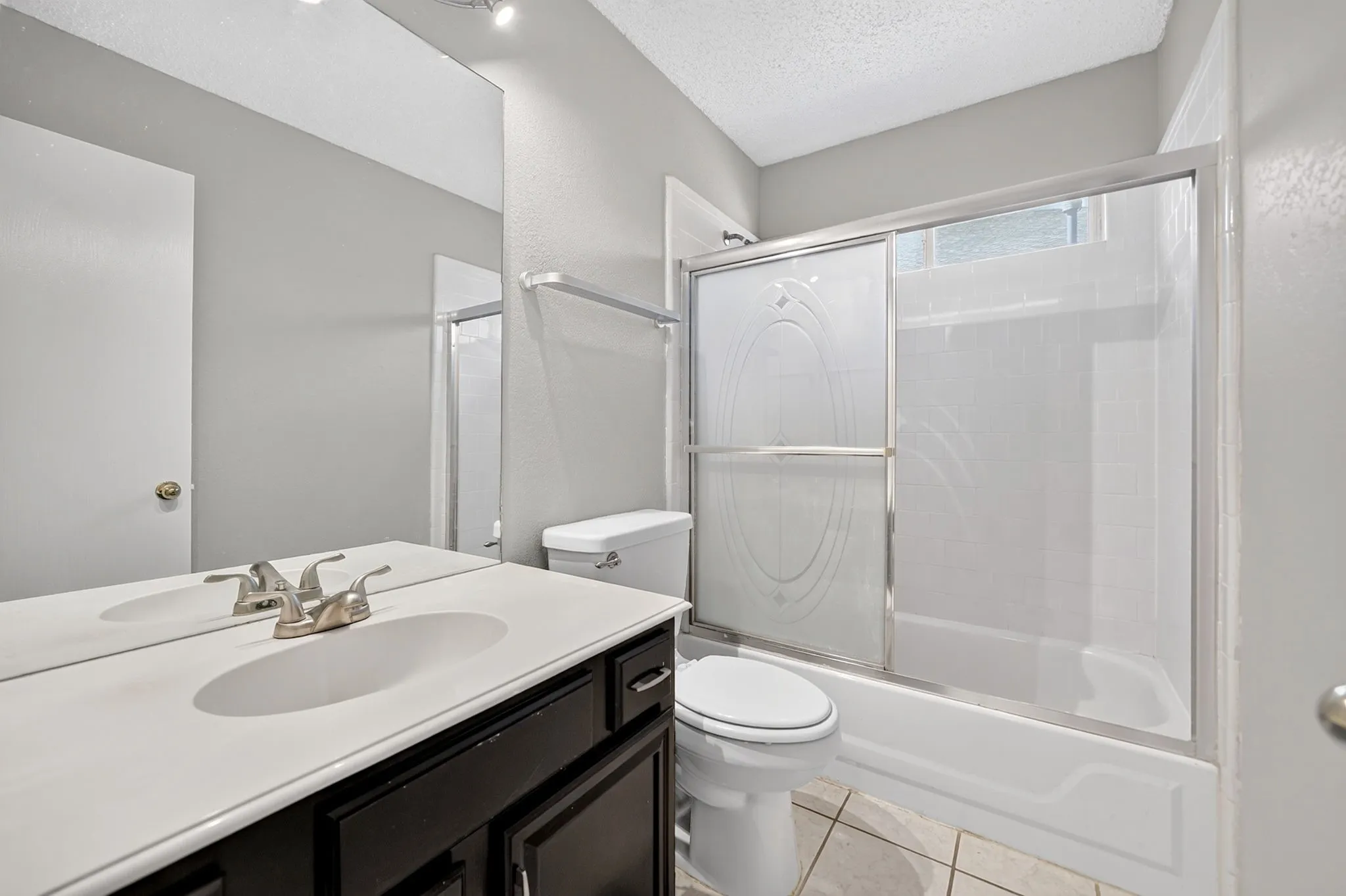 Bathroom featuring a single vanity with a white countertop, dark wood-finish cabinetry, a shower-tub combination with a sliding glass door, and neutral-toned wall paint