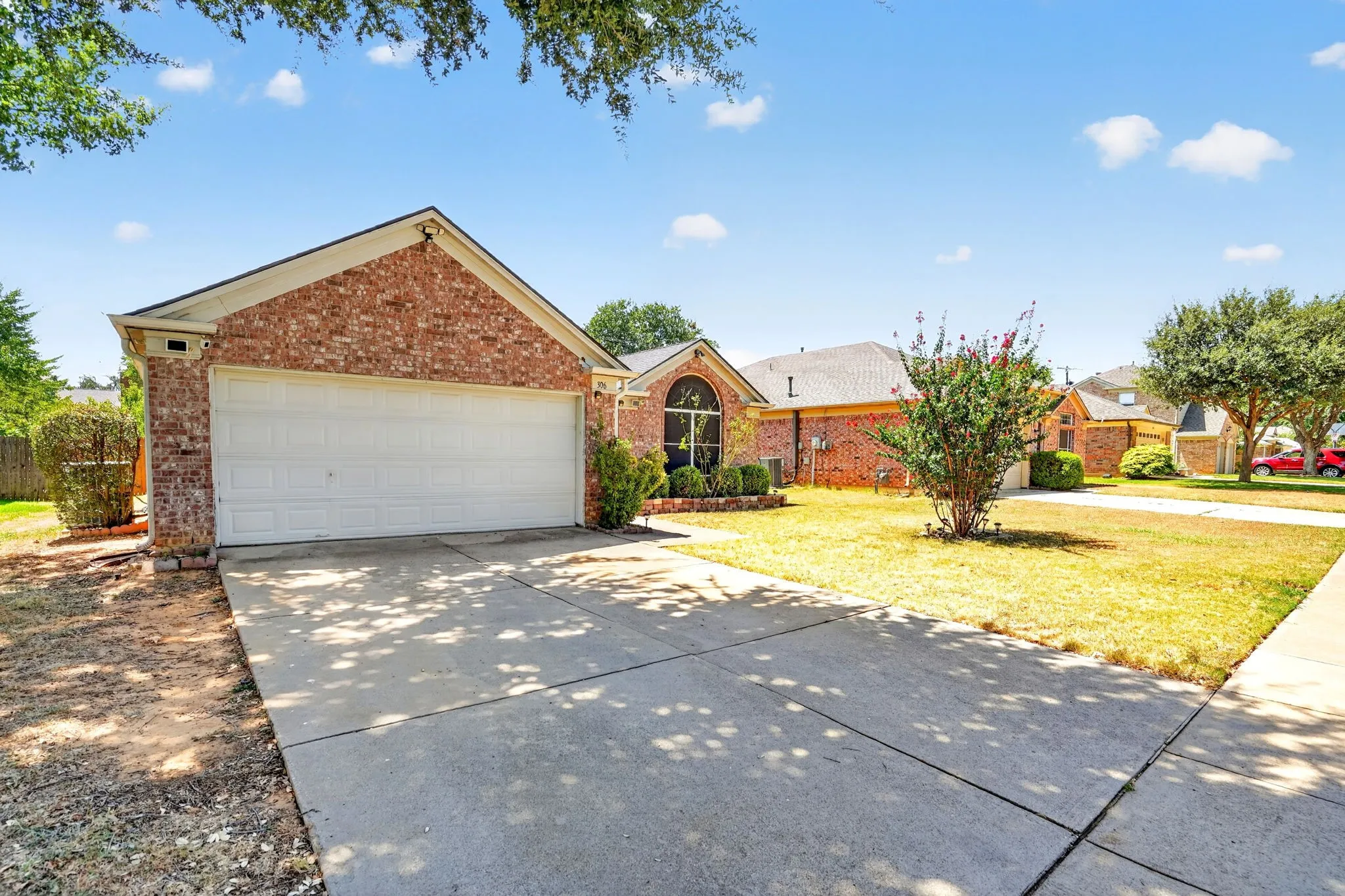 Brick exterior with an attached two-car garage, concrete driveway, and established front yard landscaping