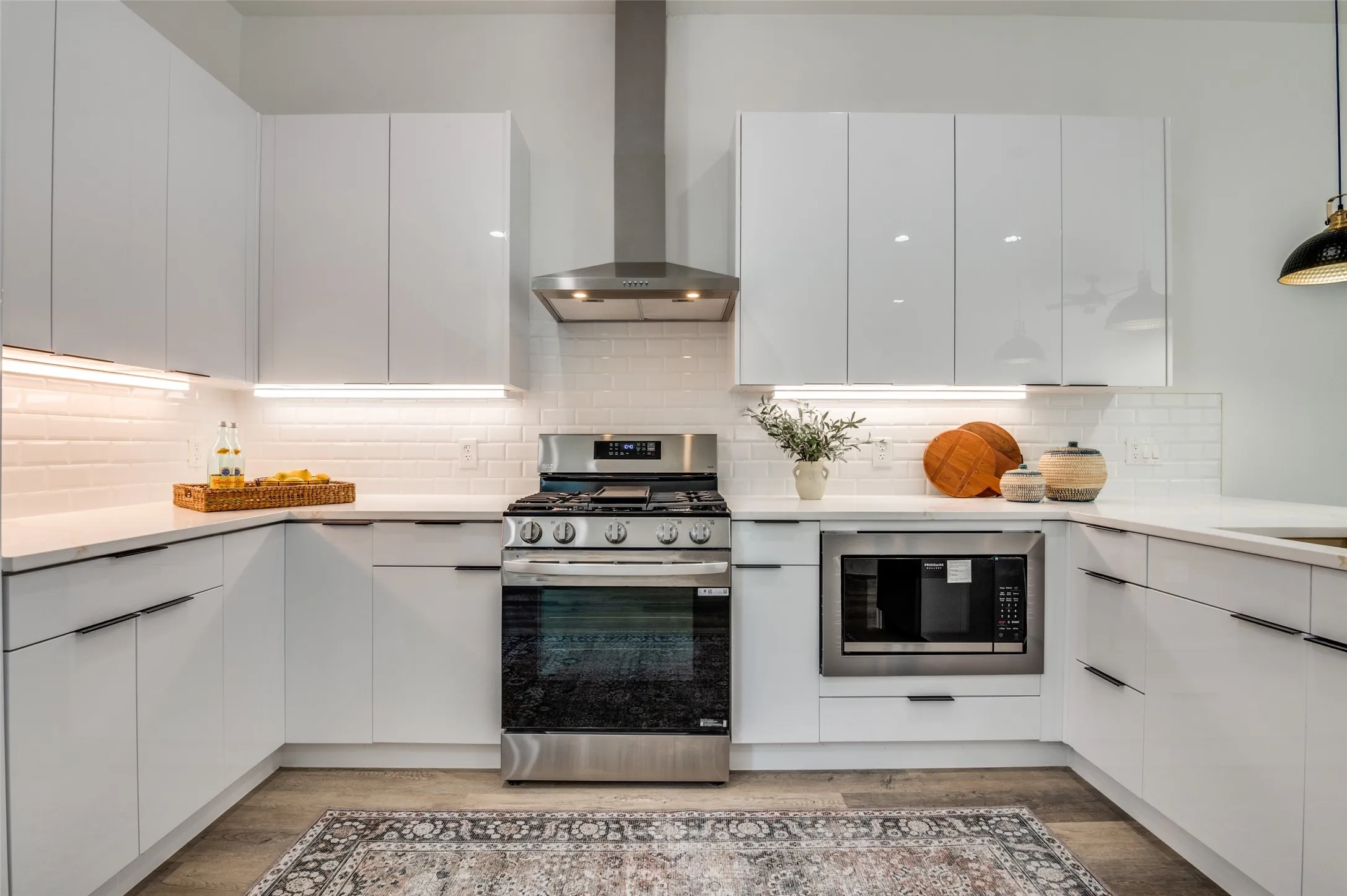 Kitchen with stainless steel gas stove, wall chimney range hood, built in microwave, and modern cabinets