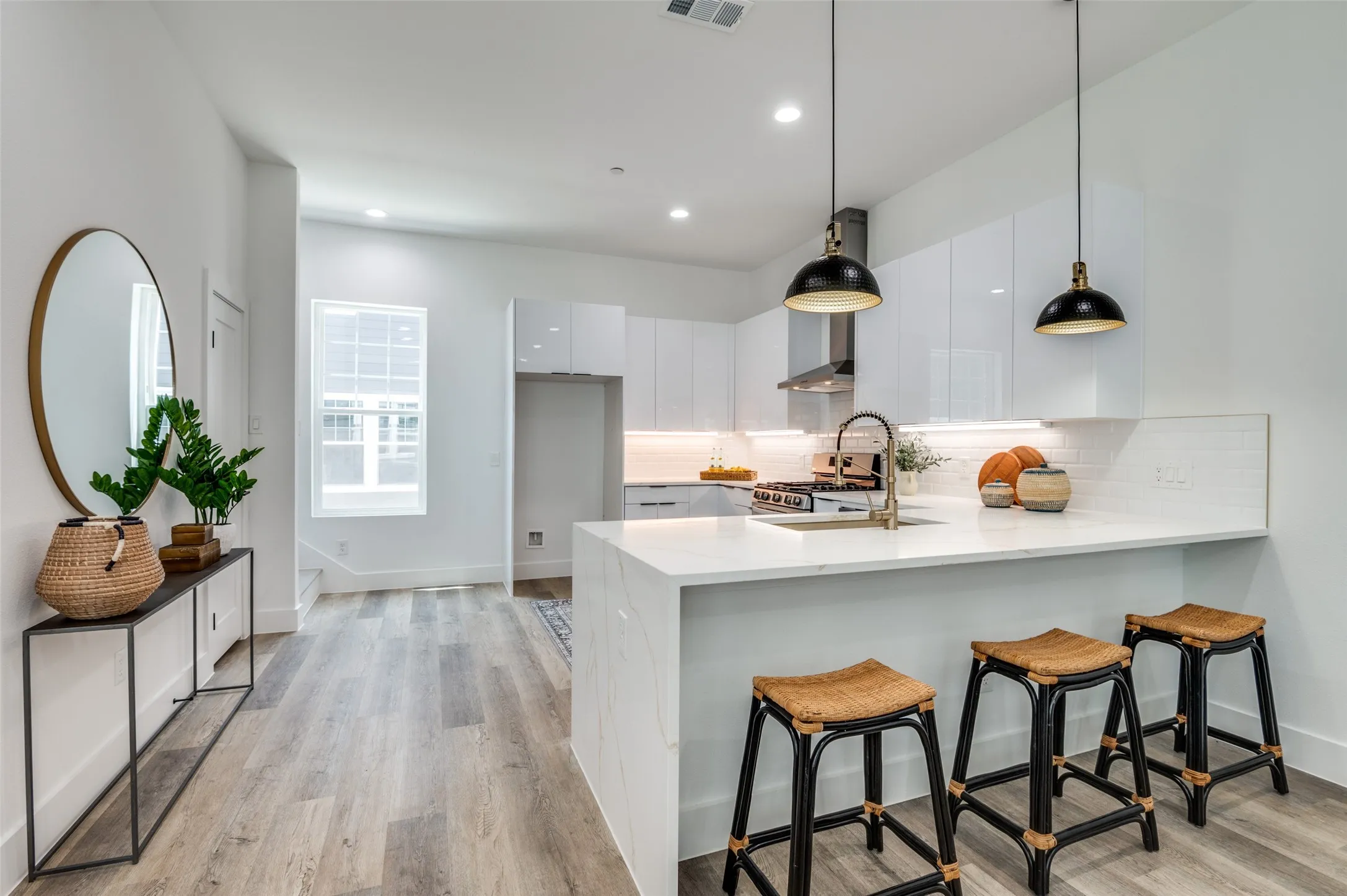 Kitchen with modern cabinets, a peninsula, white cabinets, light wood finished floors, and tasteful backsplash