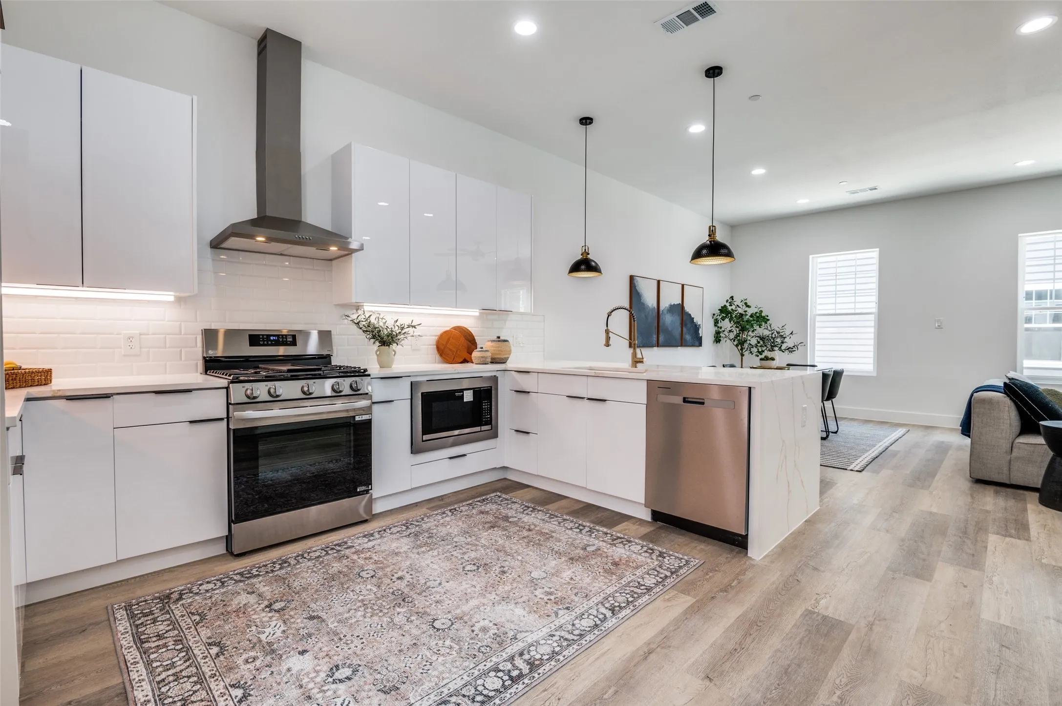 Kitchen with stainless steel appliances, wall chimney exhaust hood, modern cabinets, a peninsula, and recessed lighting
