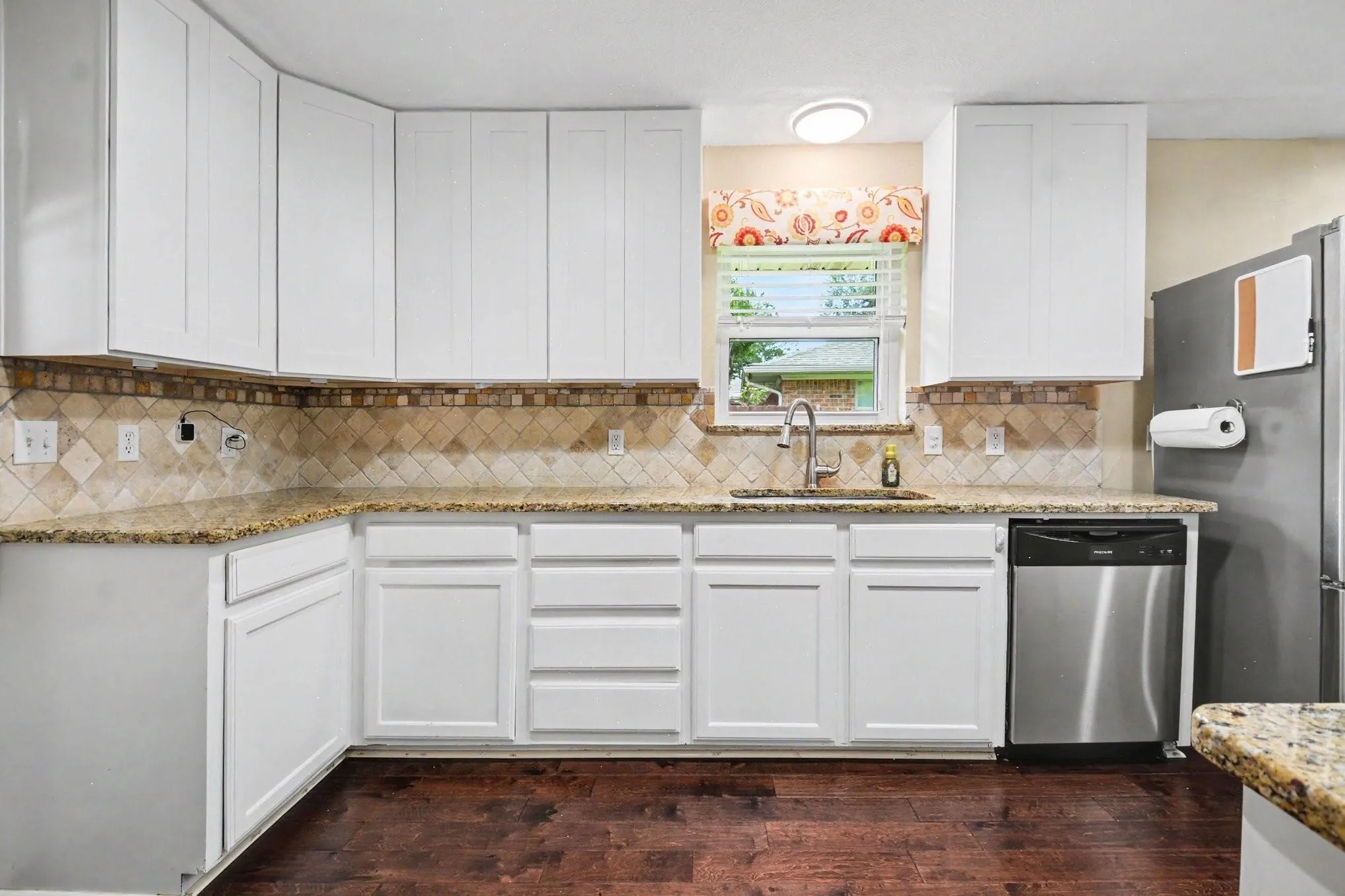 Kitchen featuring white cabinetry, granite countertops, tile backsplash, stainless steel dishwasher, and wood-finish flooring