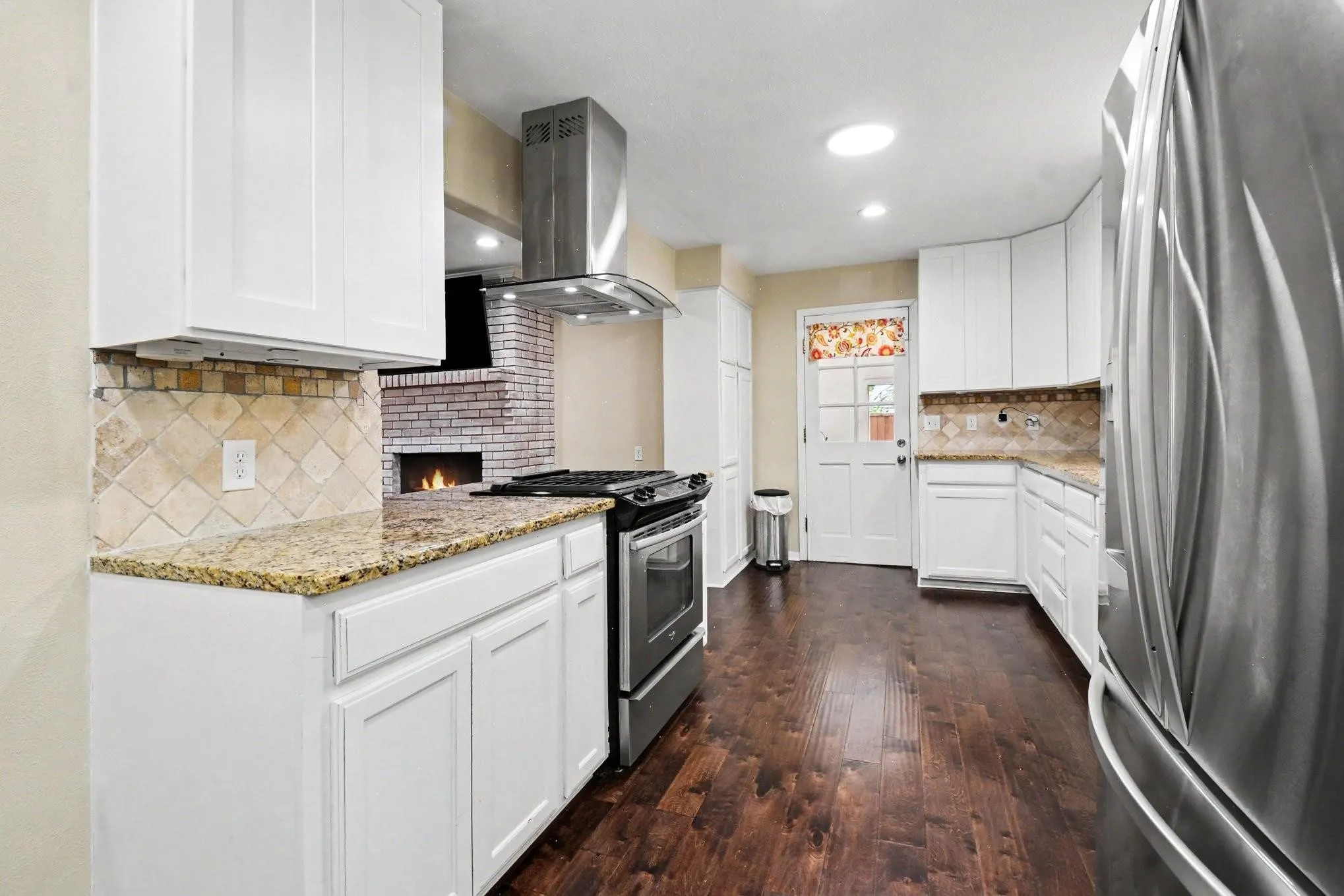 Kitchen featuring white cabinetry, granite countertops, tile backsplash, stainless steel appliances, and wood-finish flooring