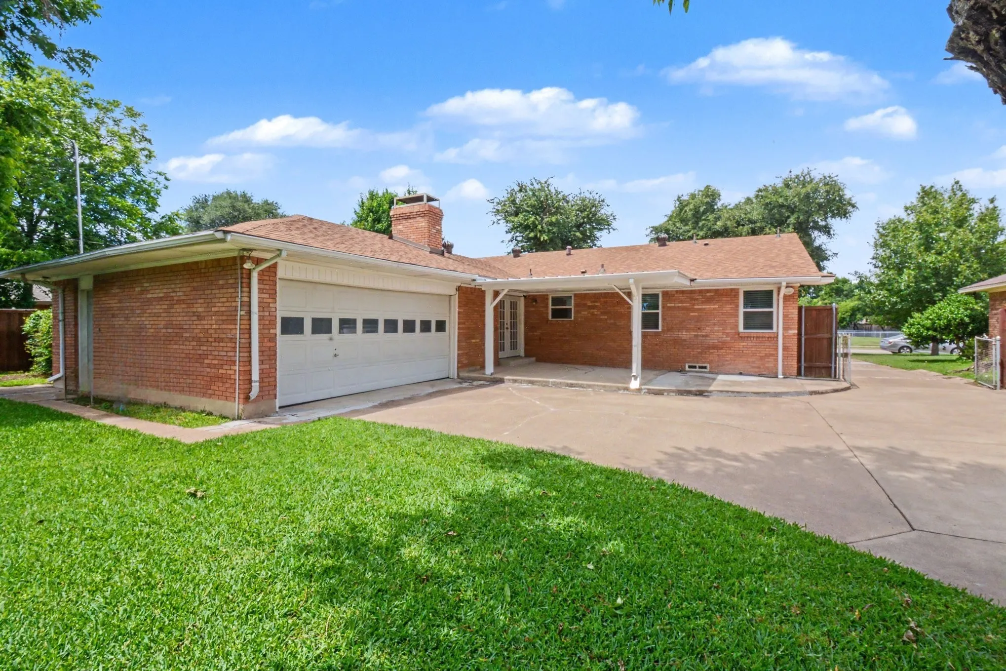 Brick exterior with an attached garage, covered patio, and a paved driveway