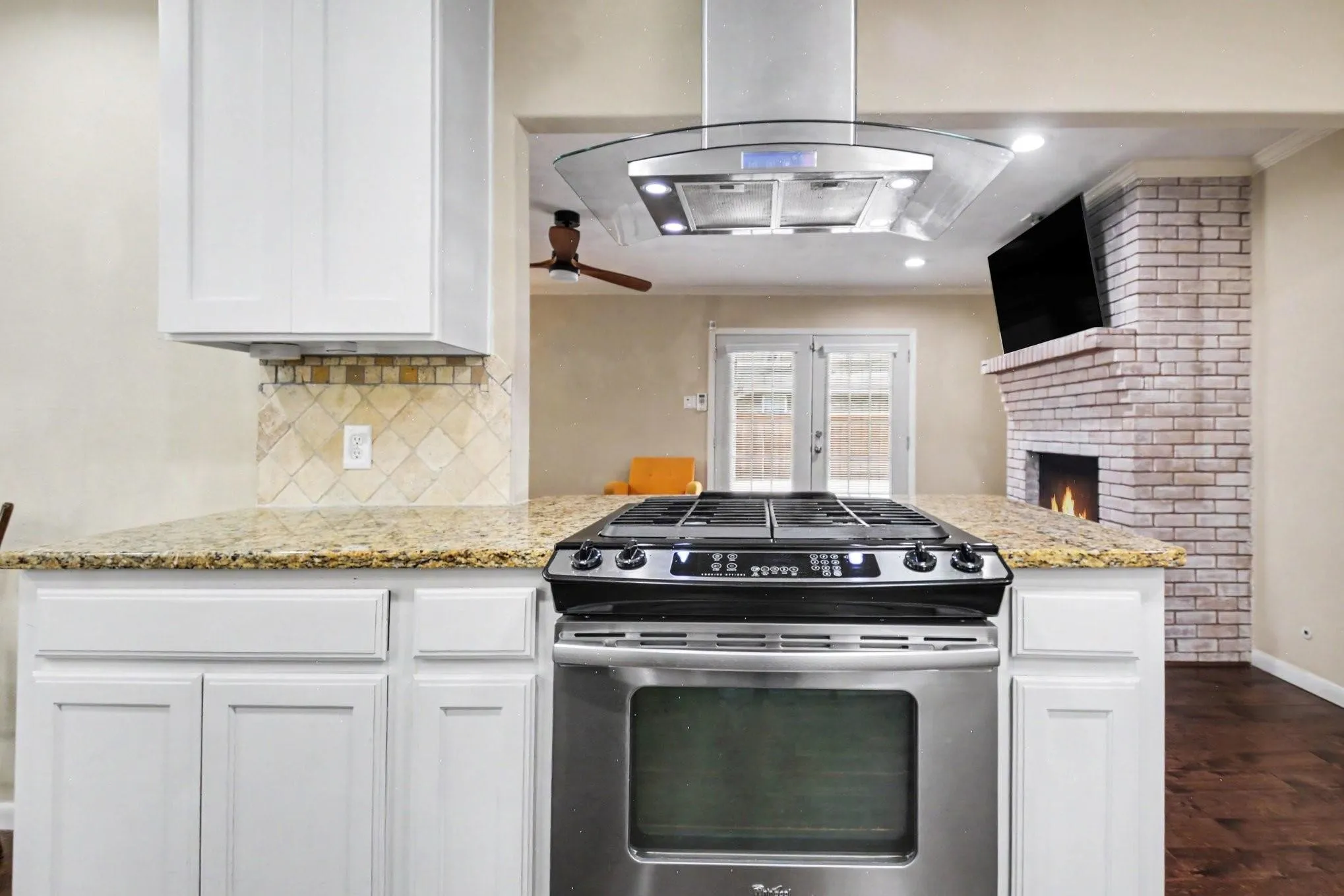 Stainless steel range with a coordinating range hood, granite countertops, white cabinetry, and a tile backsplash