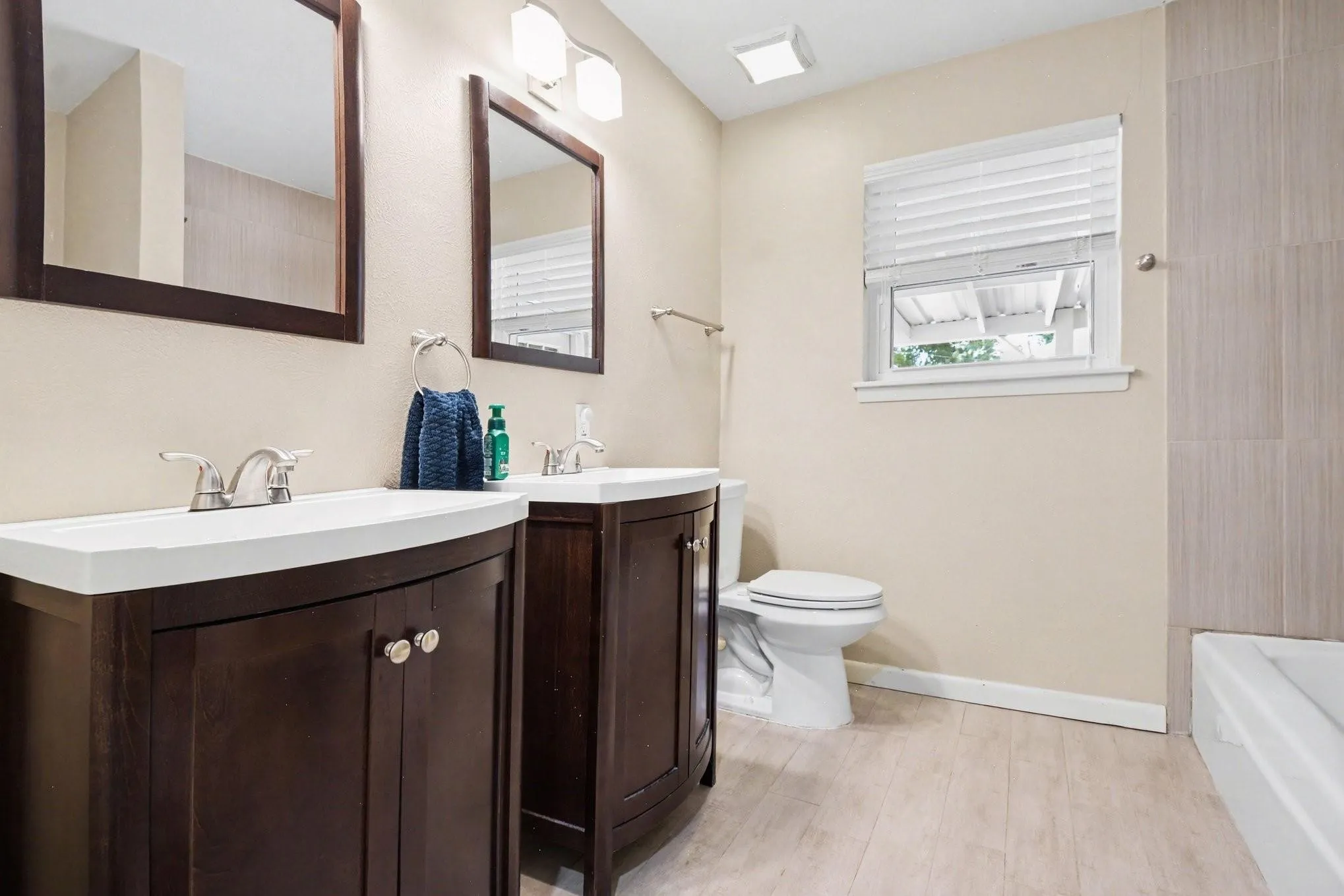 Dual wood-finish vanities with integrated sinks, brushed nickel faucets, and coordinating framed mirrors