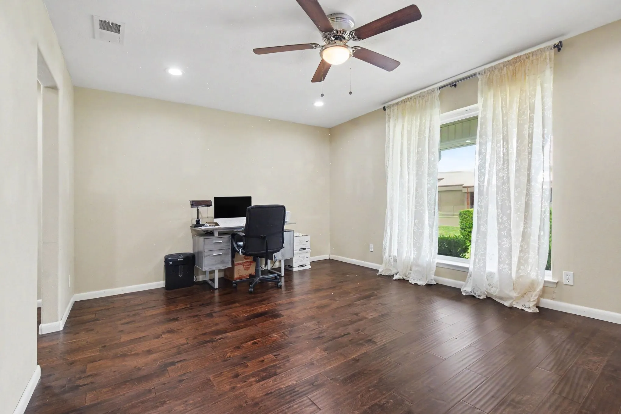 Wood-finish flooring, recessed lighting, ceiling fan with integrated light, and a large window