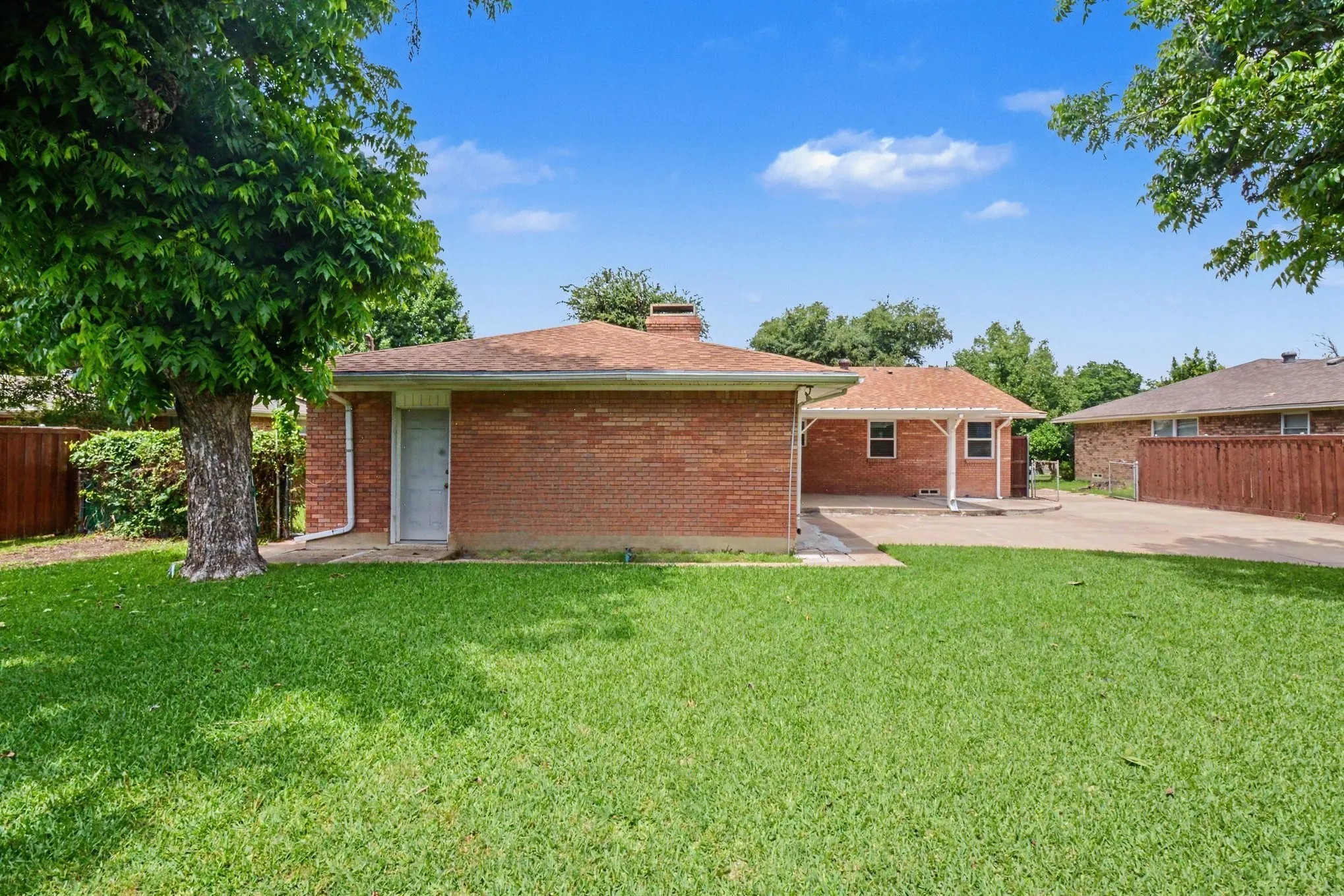 Expansive lawn, mature tree, brick exterior, covered patio, and paved driveway