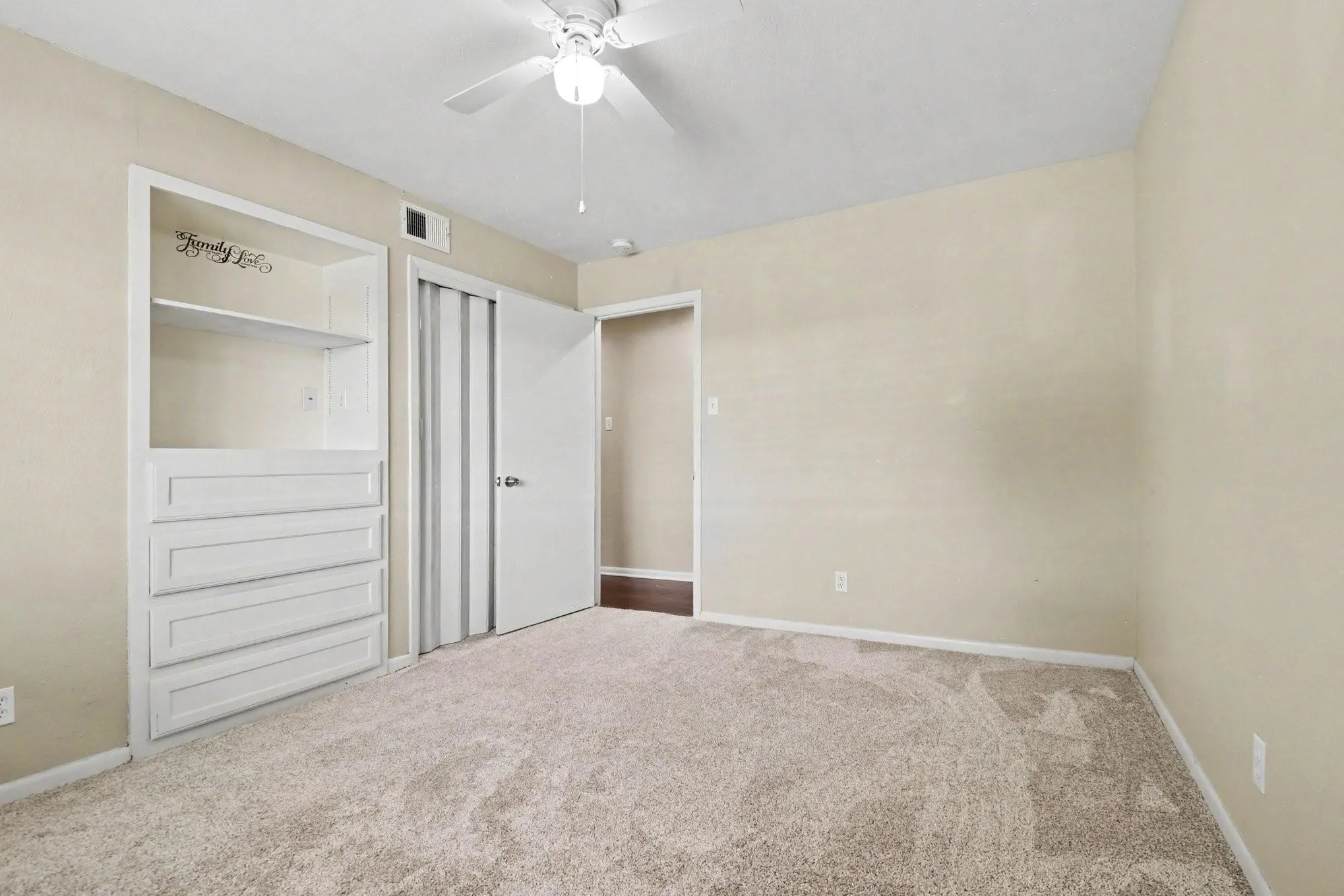 Built-in shelving and dresser unit, ceiling fan with light fixture, carpeted flooring, and a sliding closet door