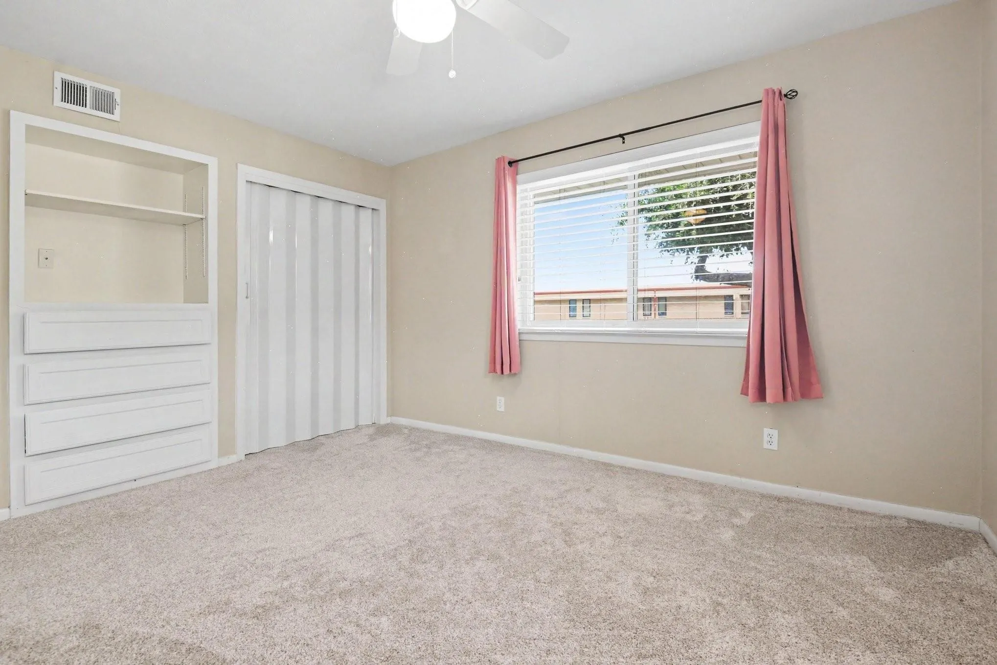 Recessed built-in shelving with drawers, accordion closet door, and light-colored carpeting