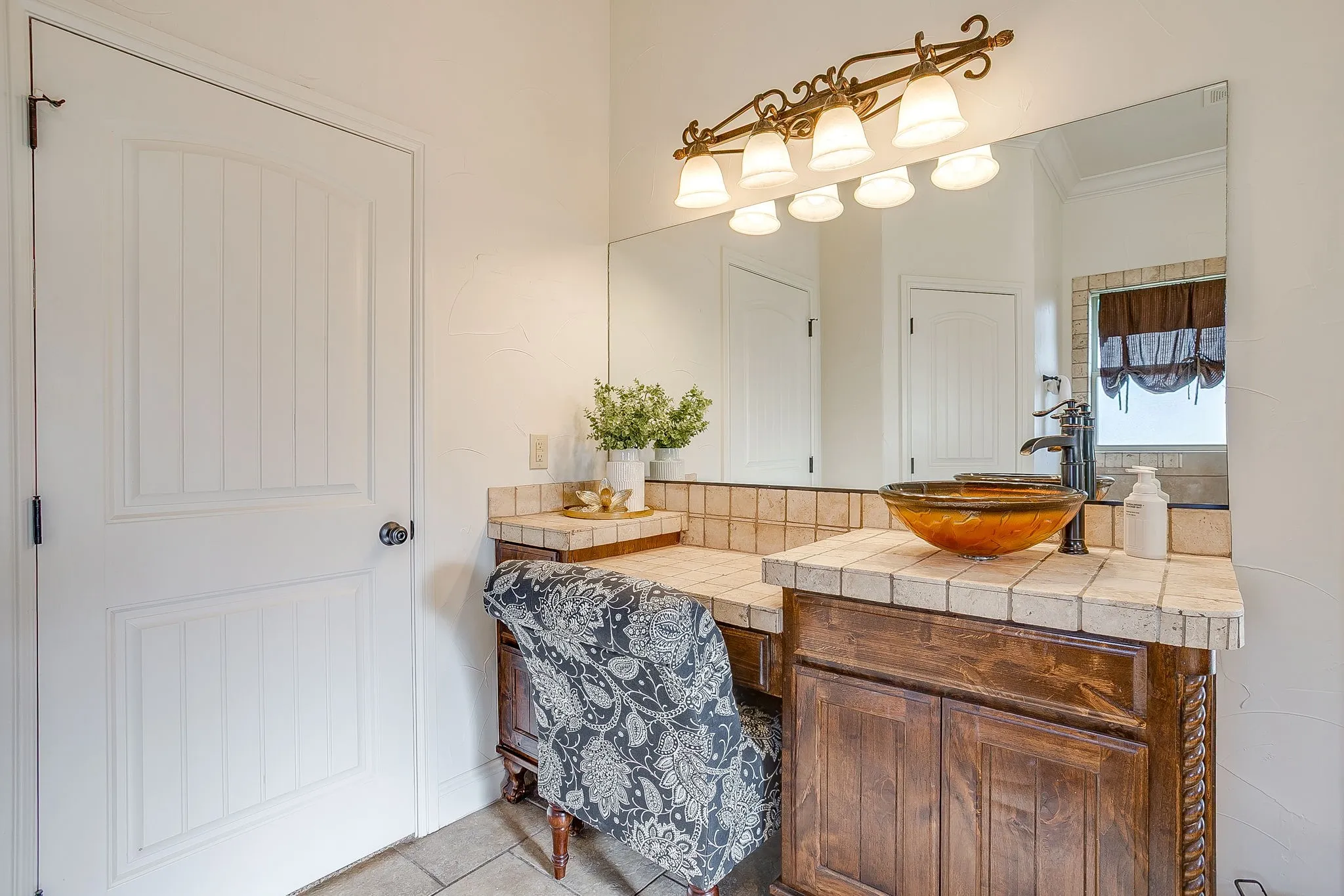 Wood-finish vanity with carved details, tile countertop, and an amber glass vessel sink