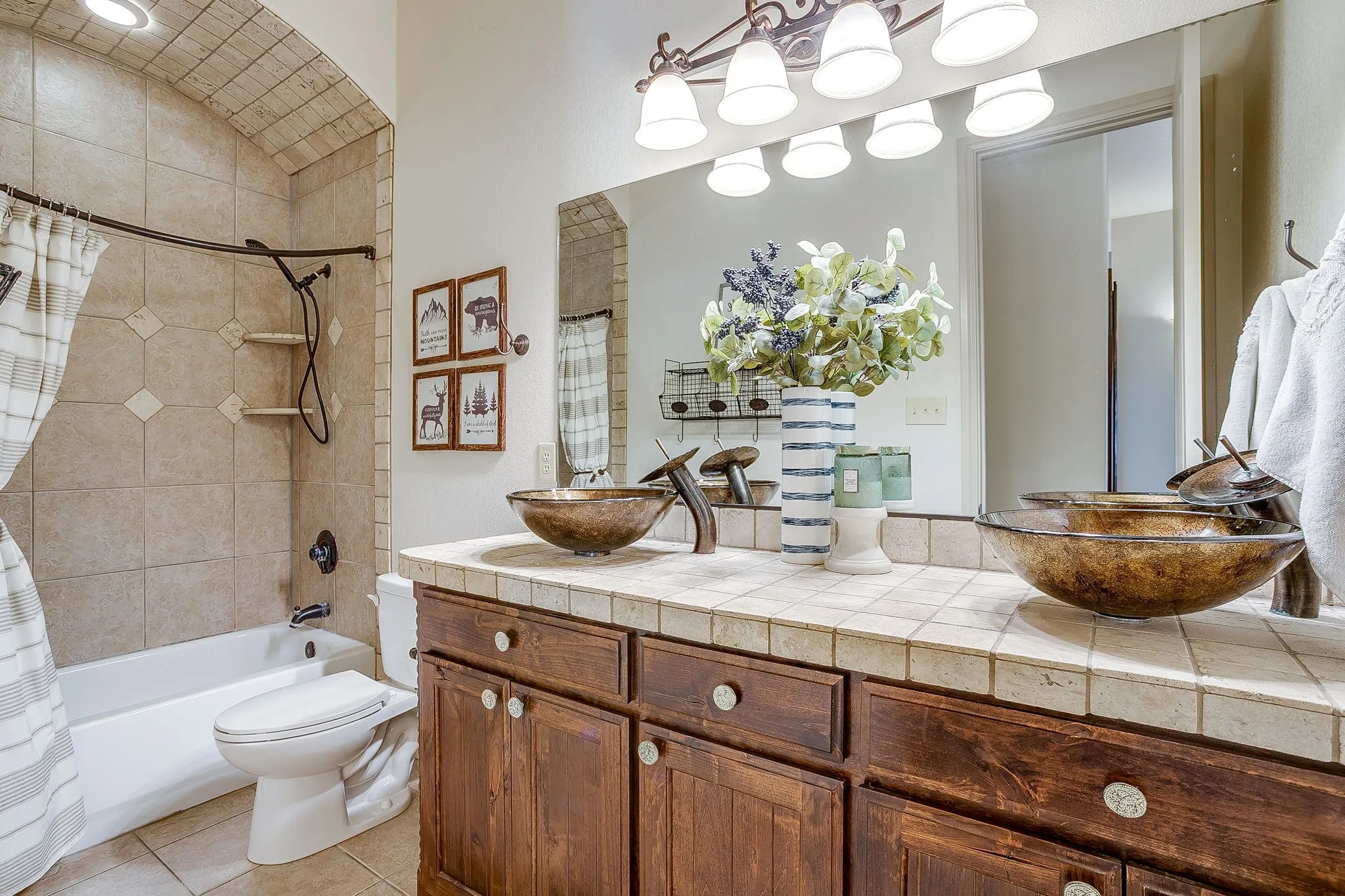 Dual vessel sinks set atop a wood-finish vanity with a tiled countertop