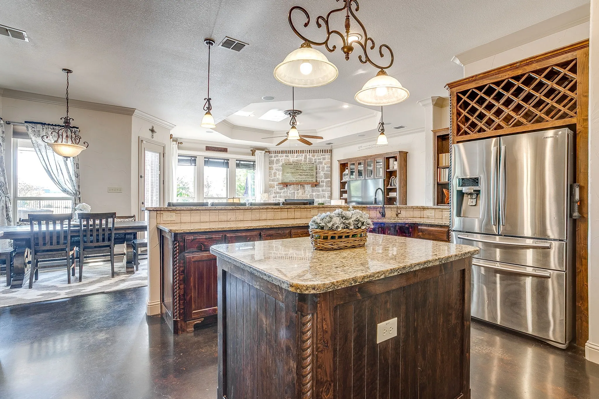 Kitchen island with a granite countertop, built-in wine storage, stainless steel refrigerator, and dark wood-finish flooring