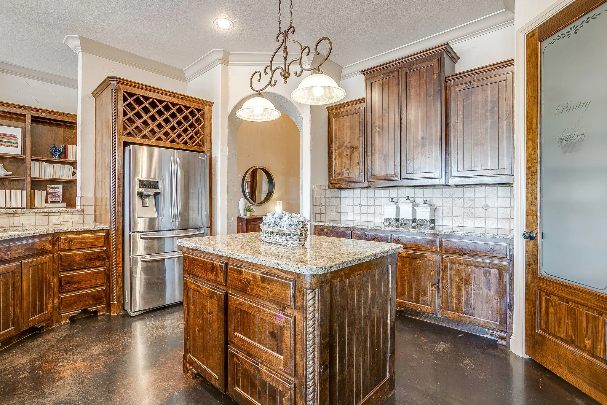 Kitchen featuring dark wood cabinetry, a central island with a granite-style countertop, stainless steel refrigerator, and a frosted pantry door