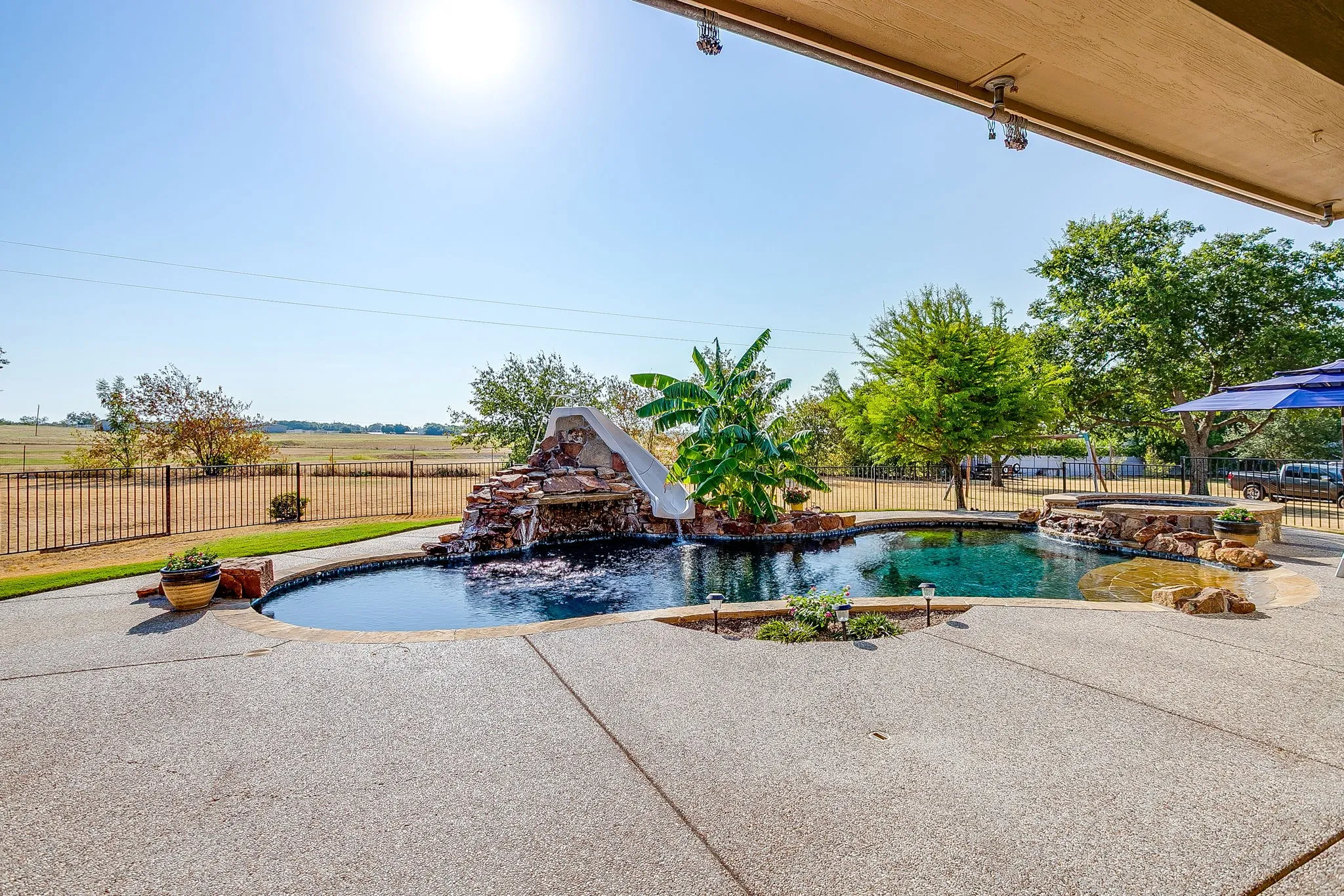 Expansive outdoor living area featuring a custom pool, rock waterfall with slide, and a separate spa