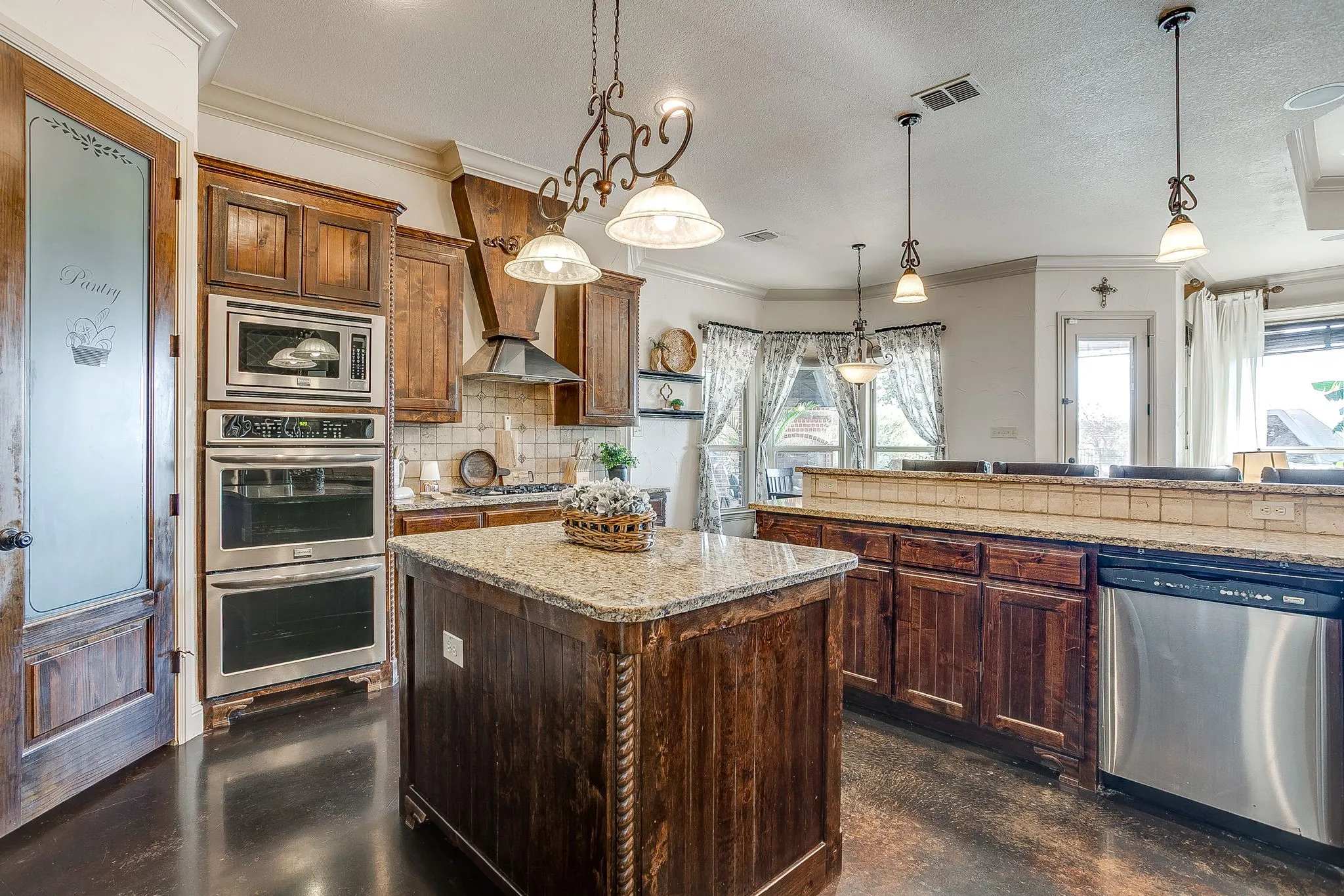 Kitchen featuring a central island with a stone countertop, dark wood-finish cabinetry, stainless steel appliances including a built-in microwave and double ovens, and decorative pendant lighting