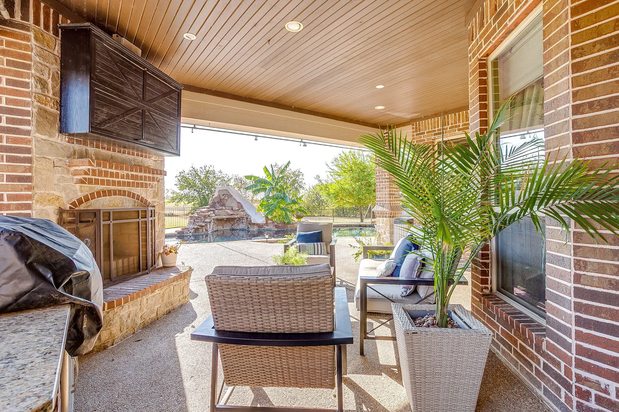 Covered outdoor patio featuring a brick and stone fireplace, built-in cabinetry with a stone countertop, and recessed lighting