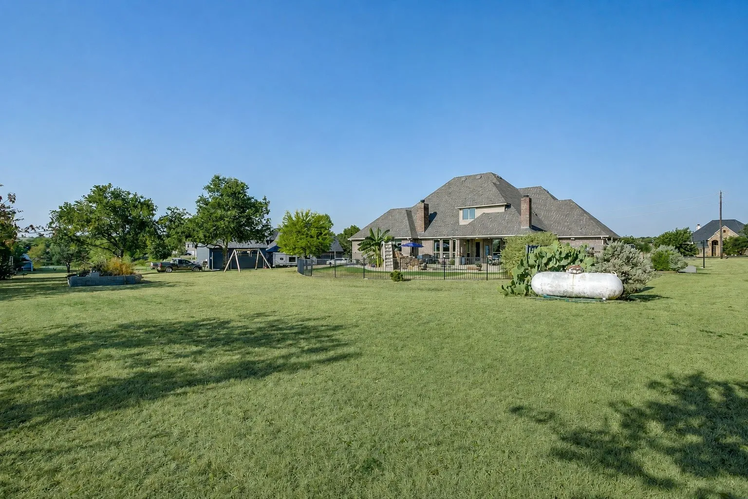 Expansive green lawn with mature trees and a brick-clad residence featuring a multi-gabled roofline