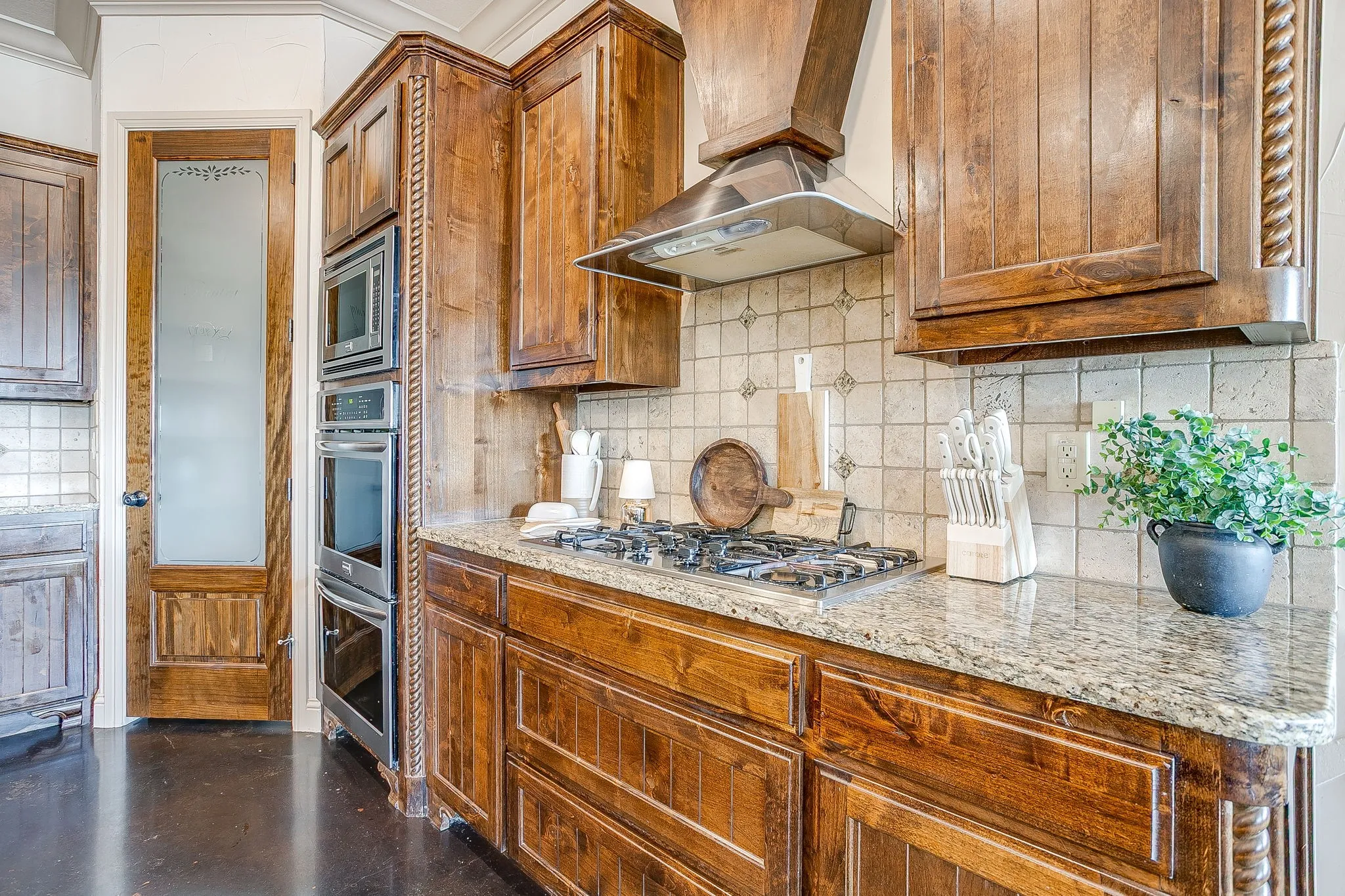 Custom wood cabinetry, stainless steel appliances, granite countertops, gas cooktop, and tile backsplash