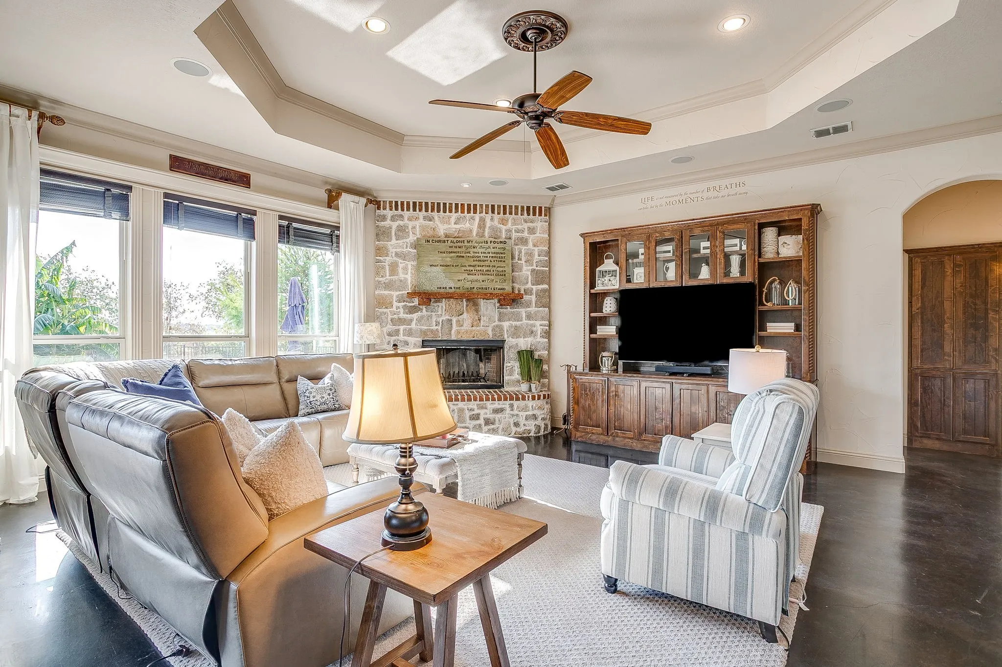 Spacious living area featuring a stone-clad fireplace, built-in entertainment center, coffered ceiling with recessed lighting, and large windows