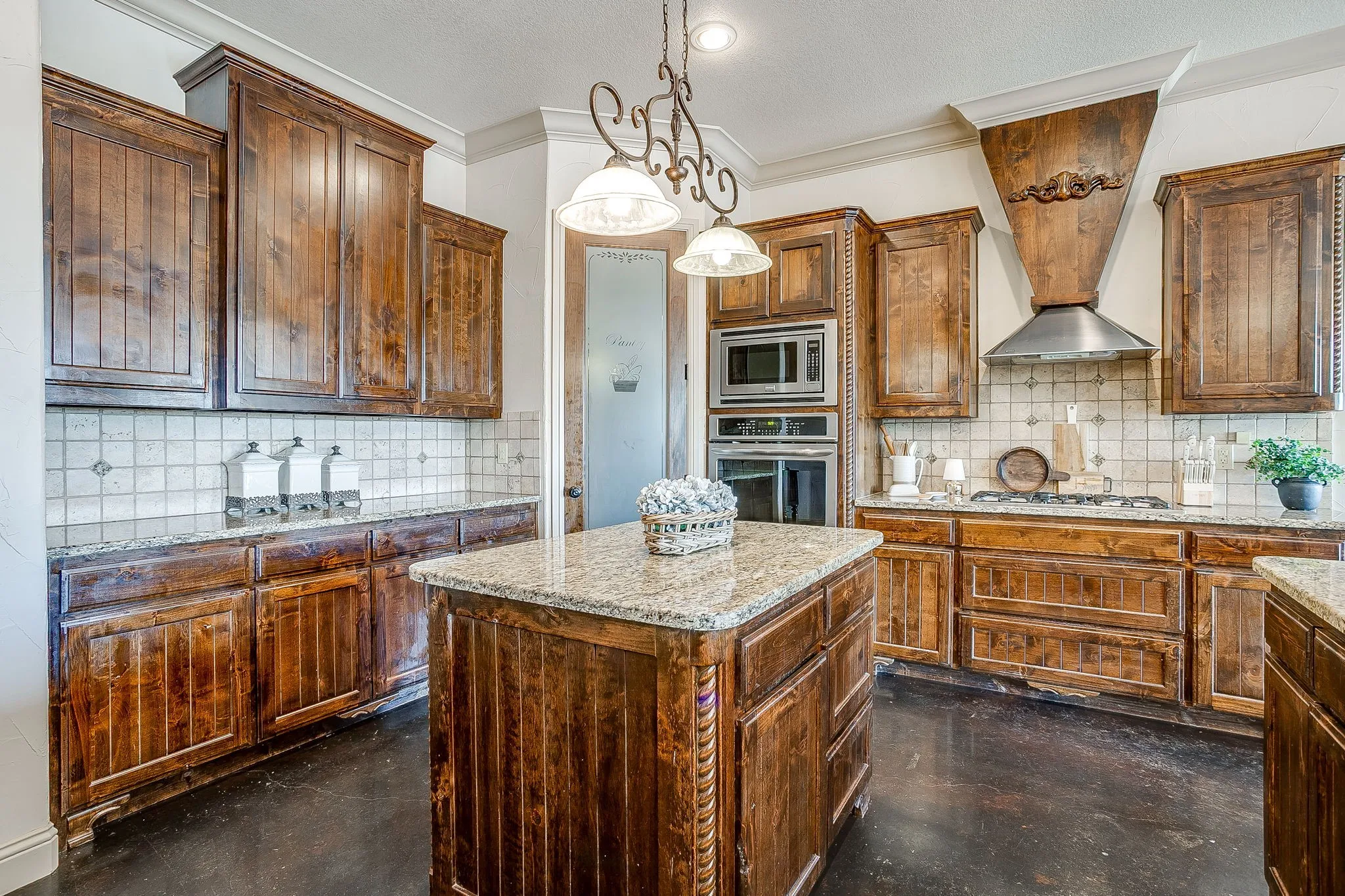 Kitchen featuring rich wood cabinetry, granite countertops, tile backsplash, built-in stainless steel appliances, and a gas cooktop with a custom wood vent hood