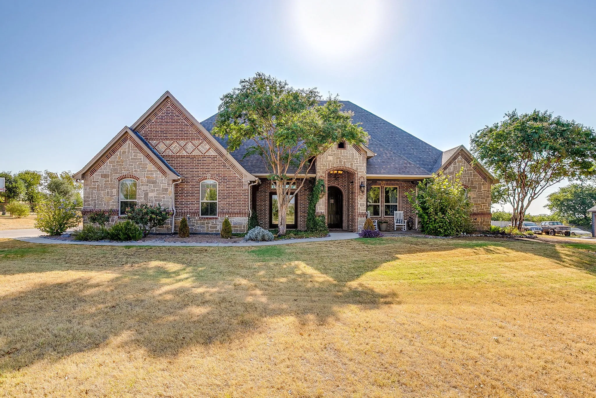 Brick and stone exterior with arched entryways, a gabled roof, and established landscaping