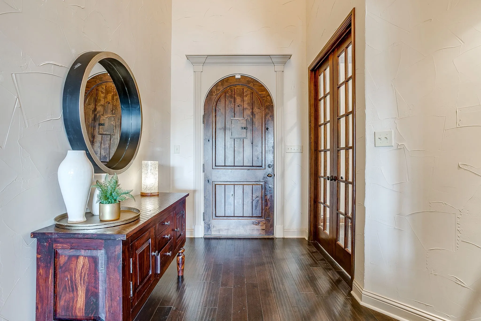 Arched wood entry door with ornate detailing, wood-finish flooring, textured walls, and wood-framed French doors
